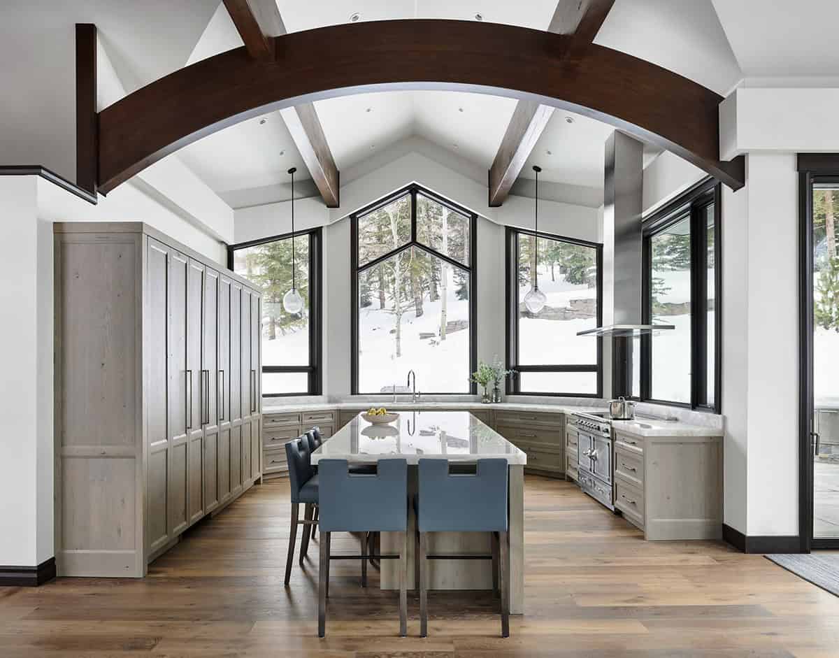 Kitchen with tall pantry cabinets, arched wood beam, and peaked window over sink