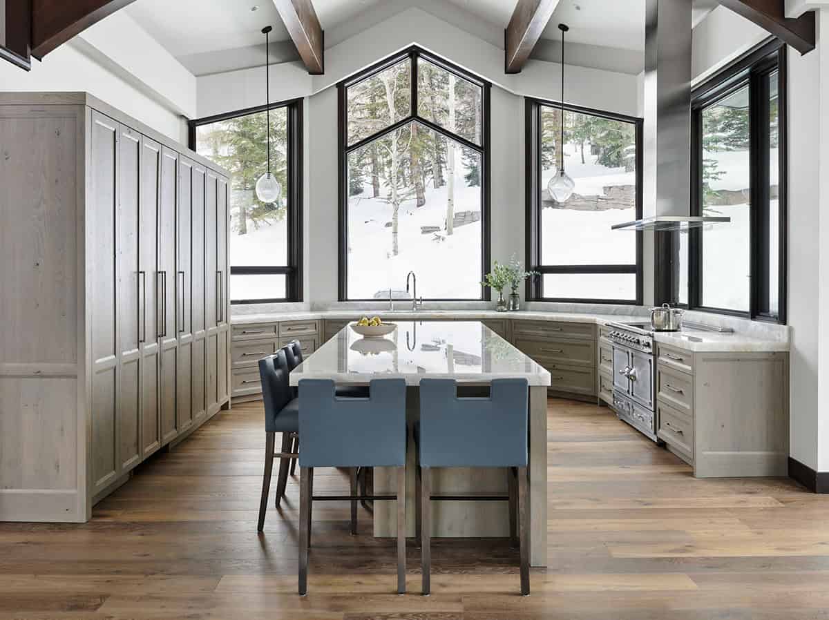 U-shaped kitchen island with blue barstools and marble countertops facing snowy windows