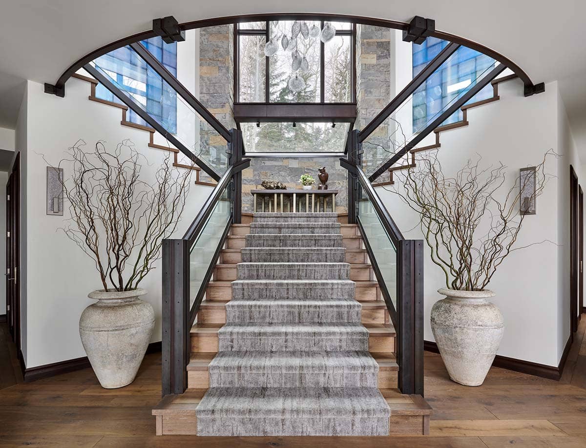 Split staircase with glass railings, large potted branches, and stone accent wall
