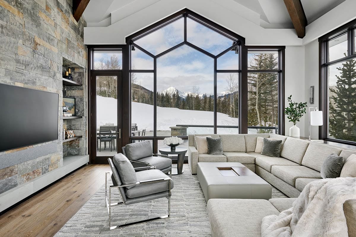 Living room with stone fireplace wall, sectional sofa, and geometric window overlooking mountains
