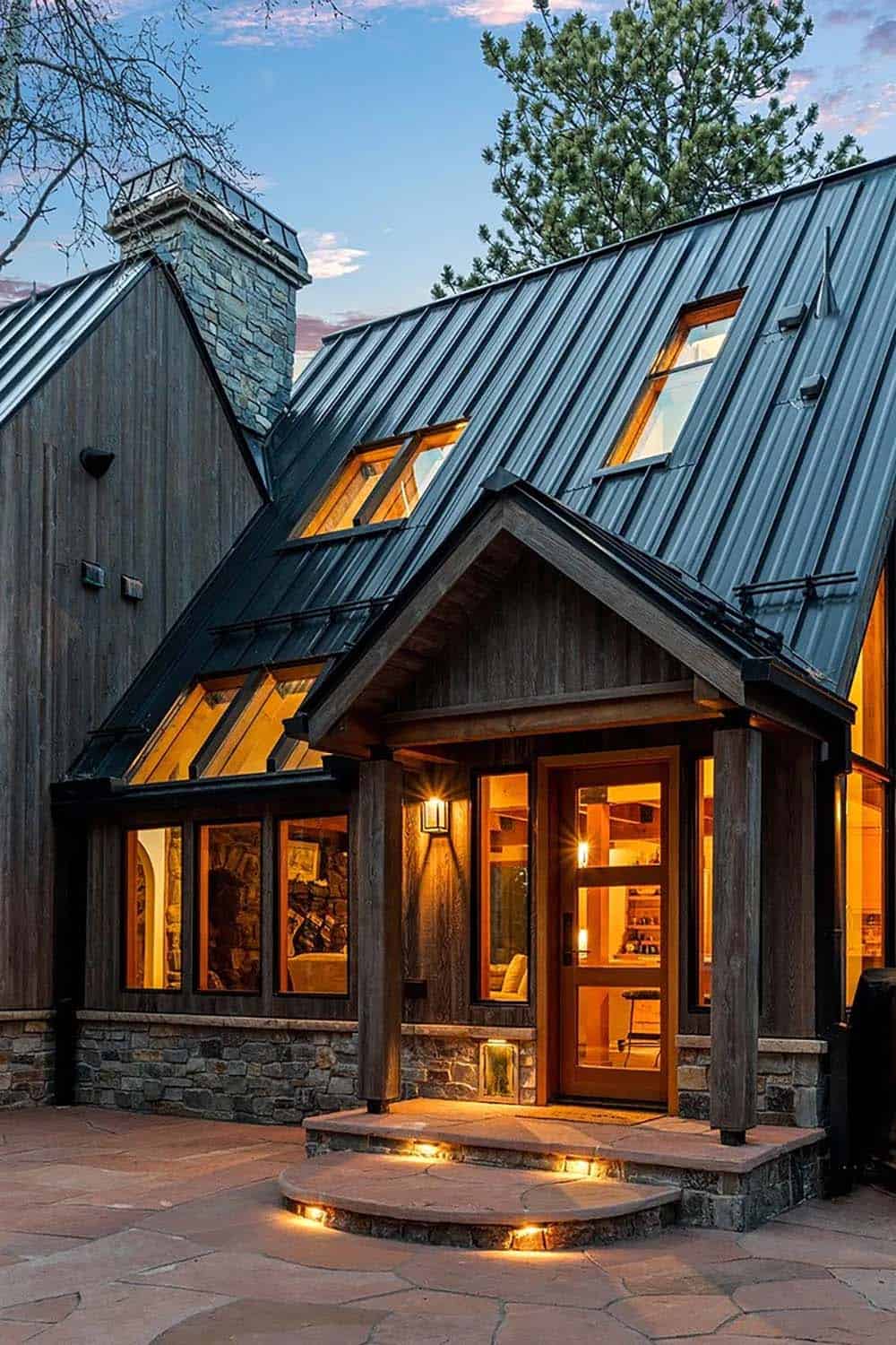 Gabled entry porch glows warm beneath a dark metal roof