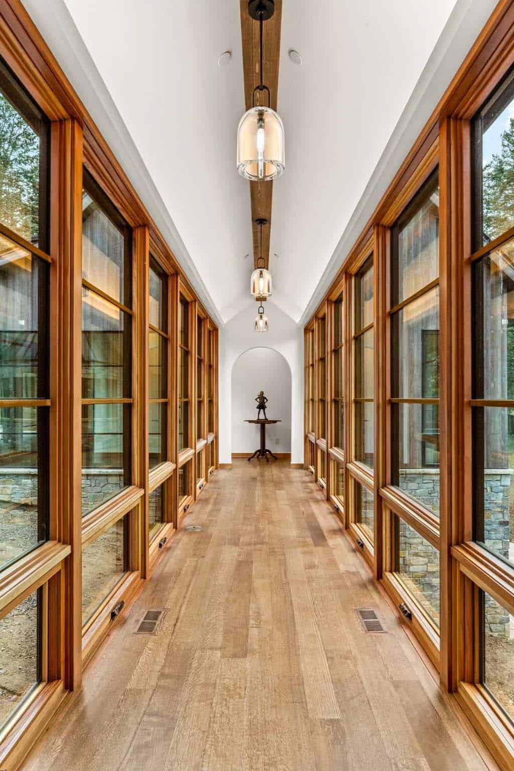 Glass-walled hallway lined with wood-framed windows leads to an archway