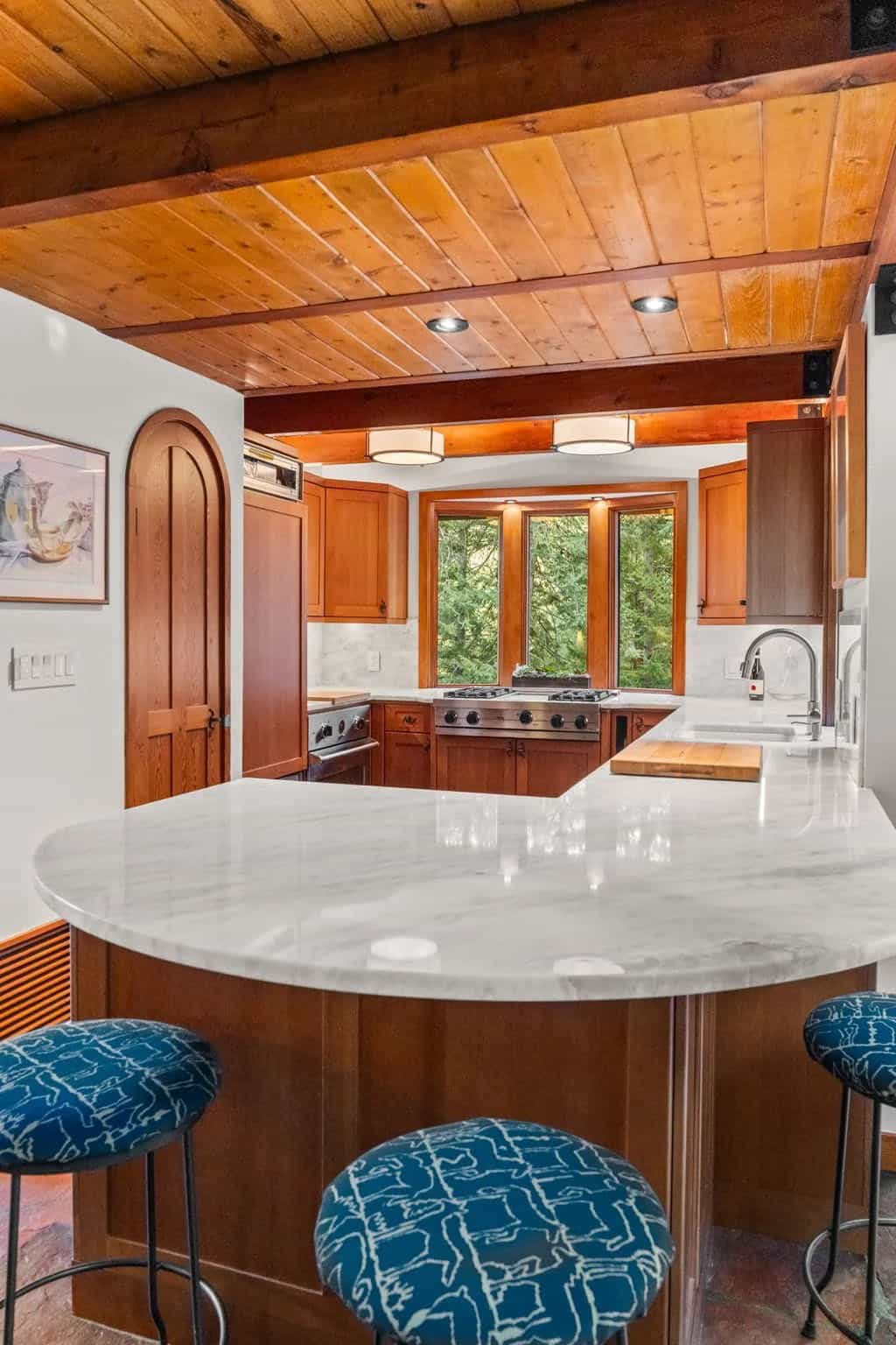 Curved marble island anchors the wood-toned kitchen with blue stools