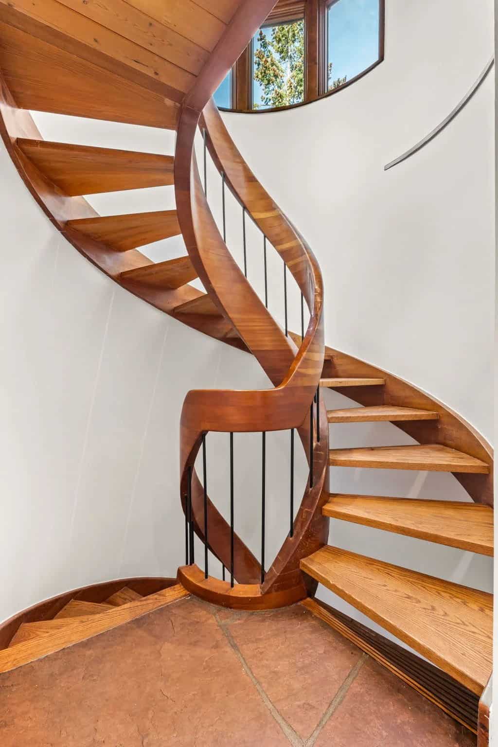 Curved wooden staircase spirals beneath a round window