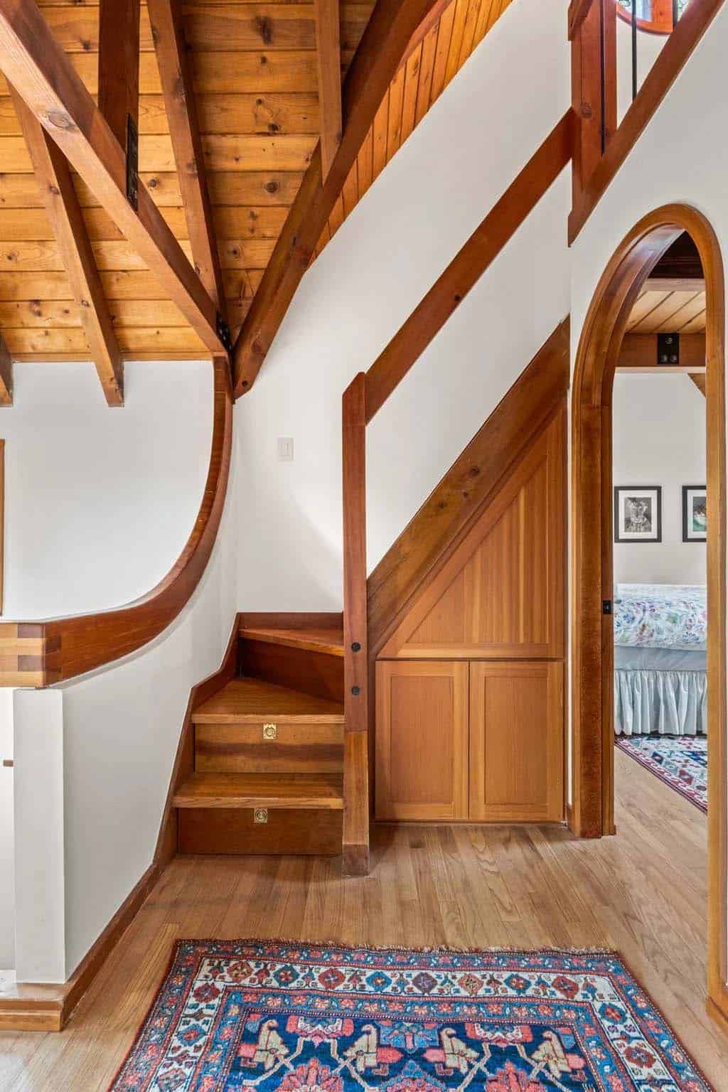 Wood staircase and paneled cabinet tuck beneath sloped timber ceiling