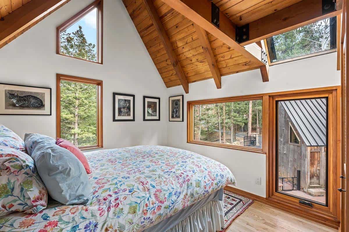 Vaulted bedroom with skylights and forest views through wood-framed windows