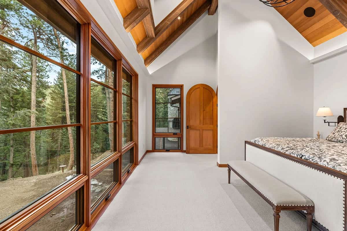 Bedroom features floor-to-ceiling windows framing dense forest views