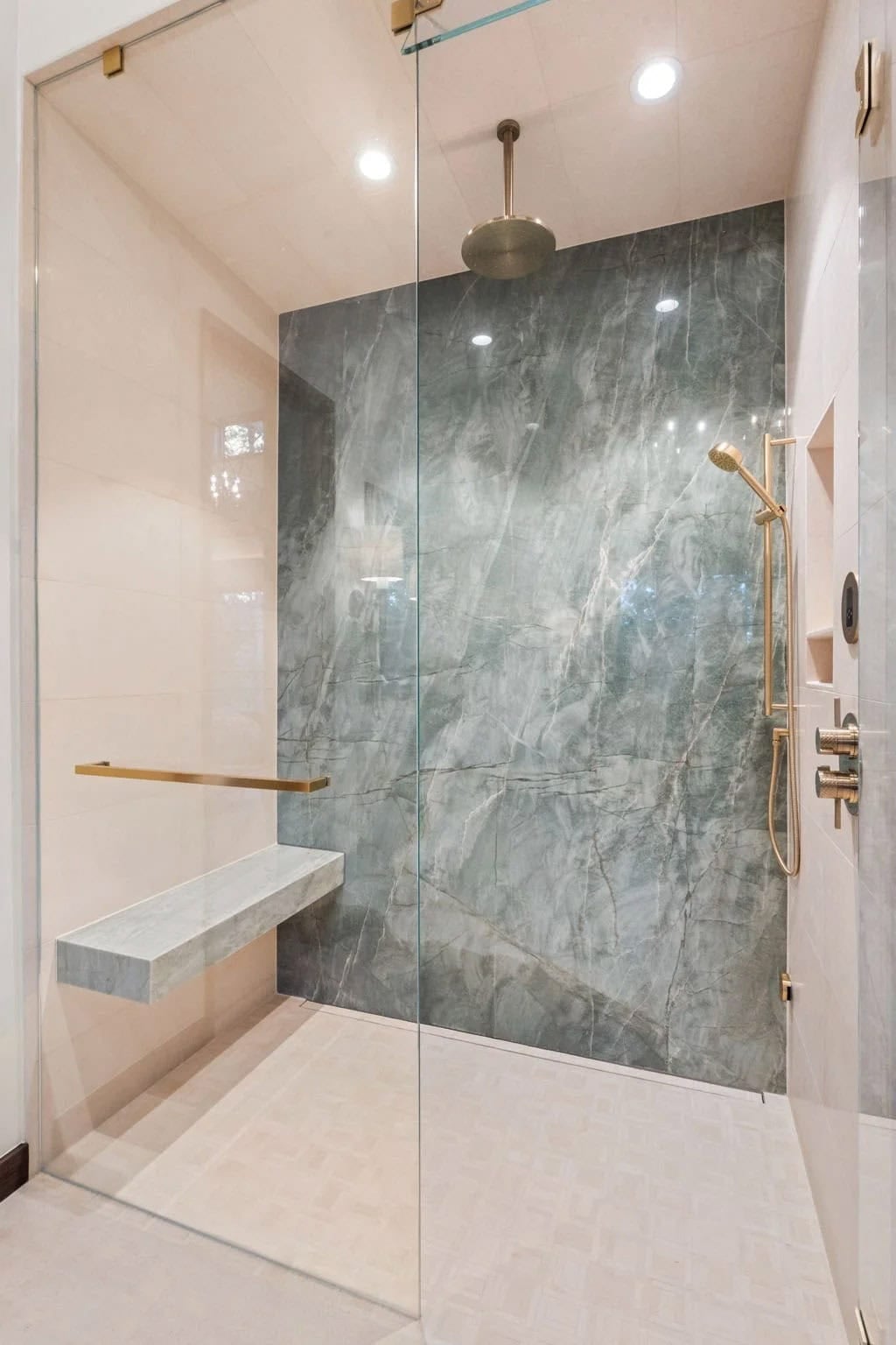 Green marble shower features a brass rain head and bench