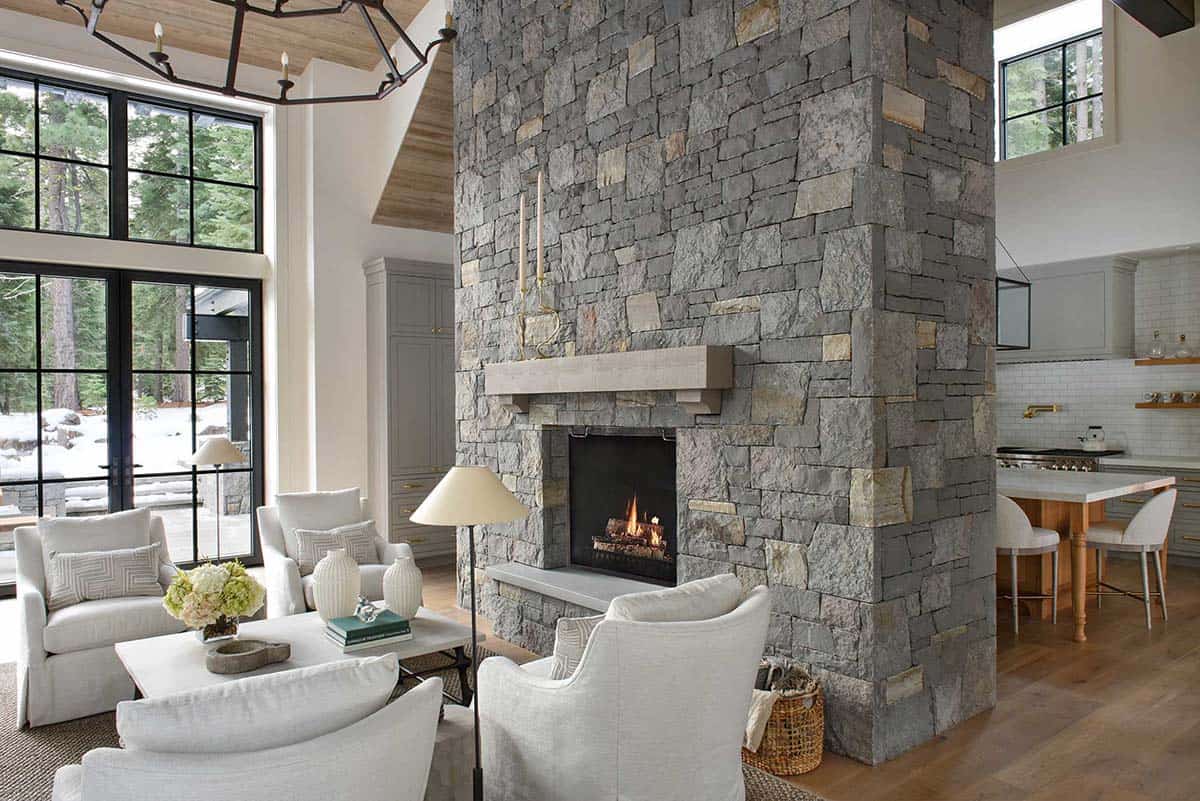 Living area with stone fireplace column opening to kitchen with pendant lighting