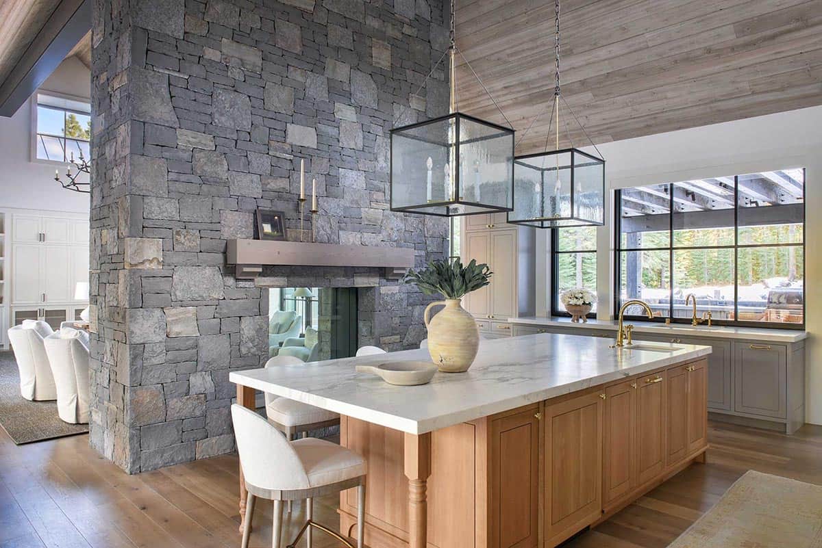 Kitchen island with marble countertop beside stone fireplace and glass pendant lights