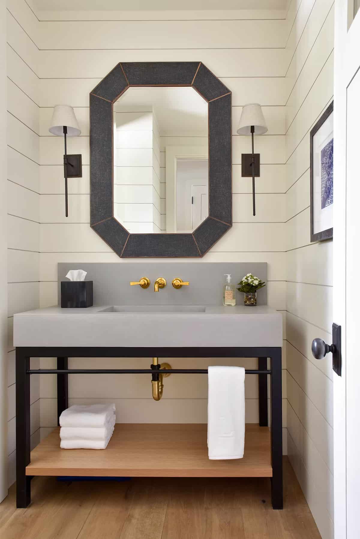 Powder room vanity with brass fixtures, sconces, and framed mirror