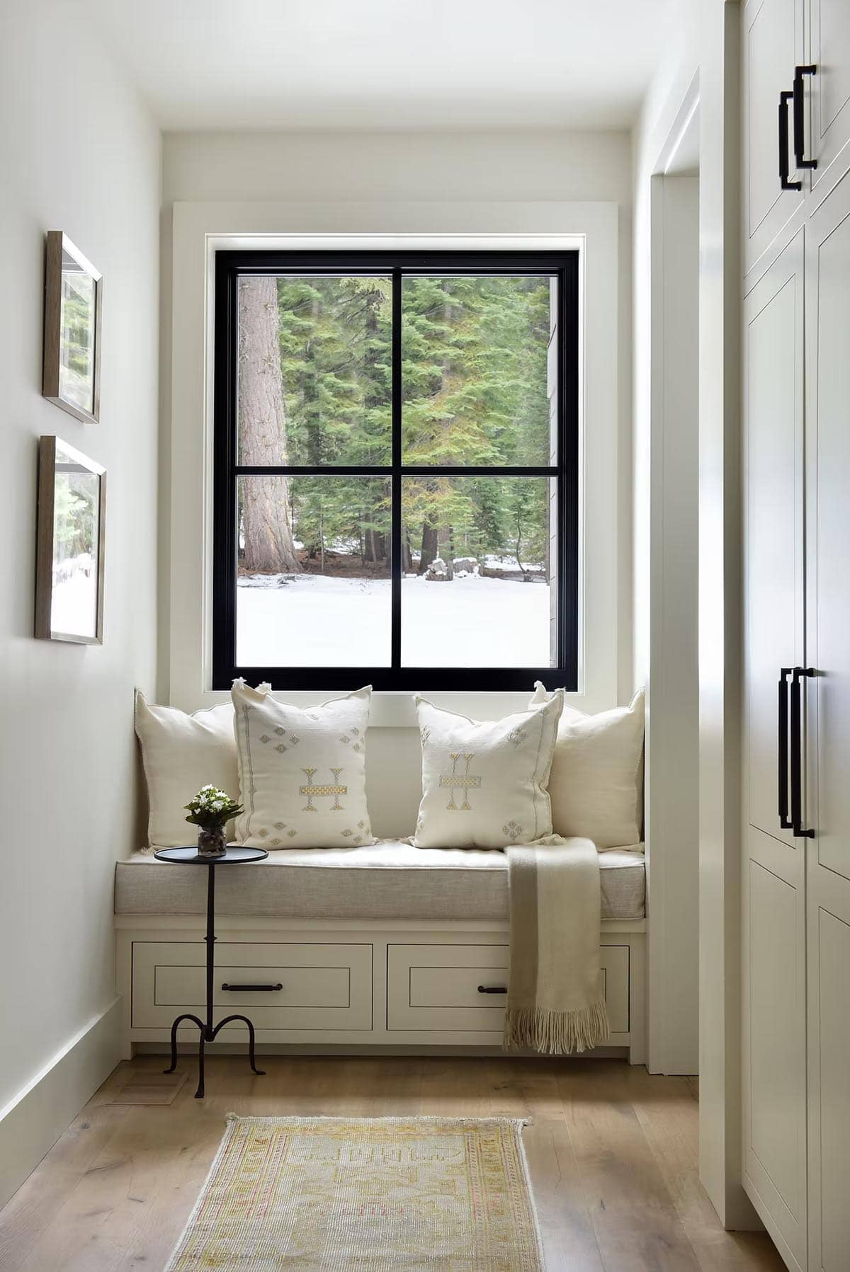 Window seat nook with patterned pillows overlooking snowy pine forest