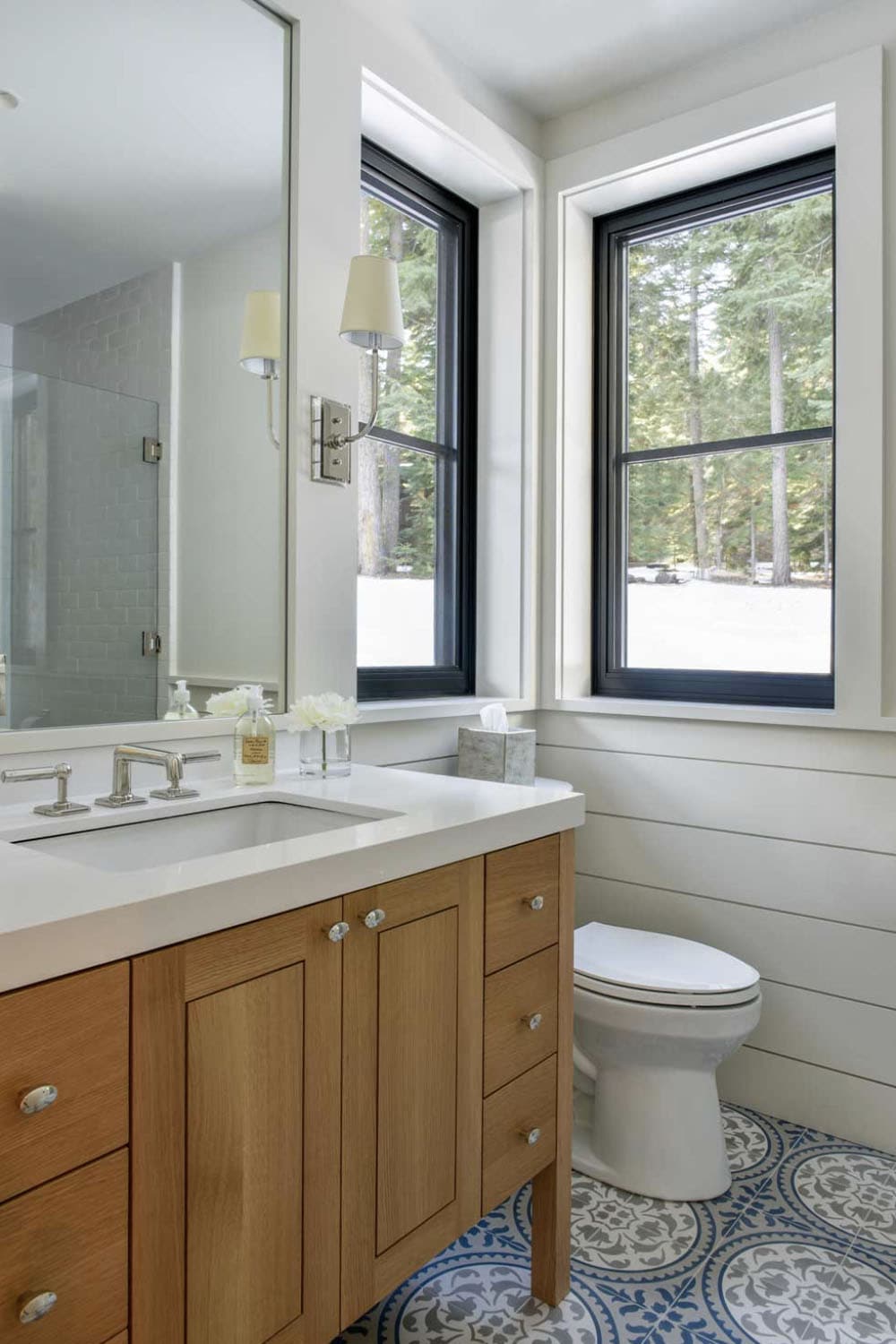 Bathroom with wood vanity, patterned tile floor, and forest-view windows