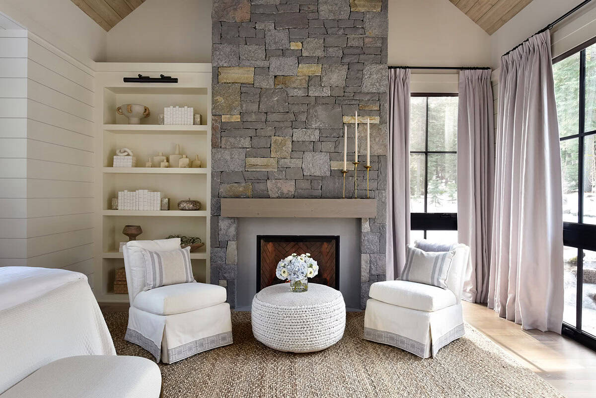 Bedroom sitting area with white armchairs, ottoman, and stone fireplace