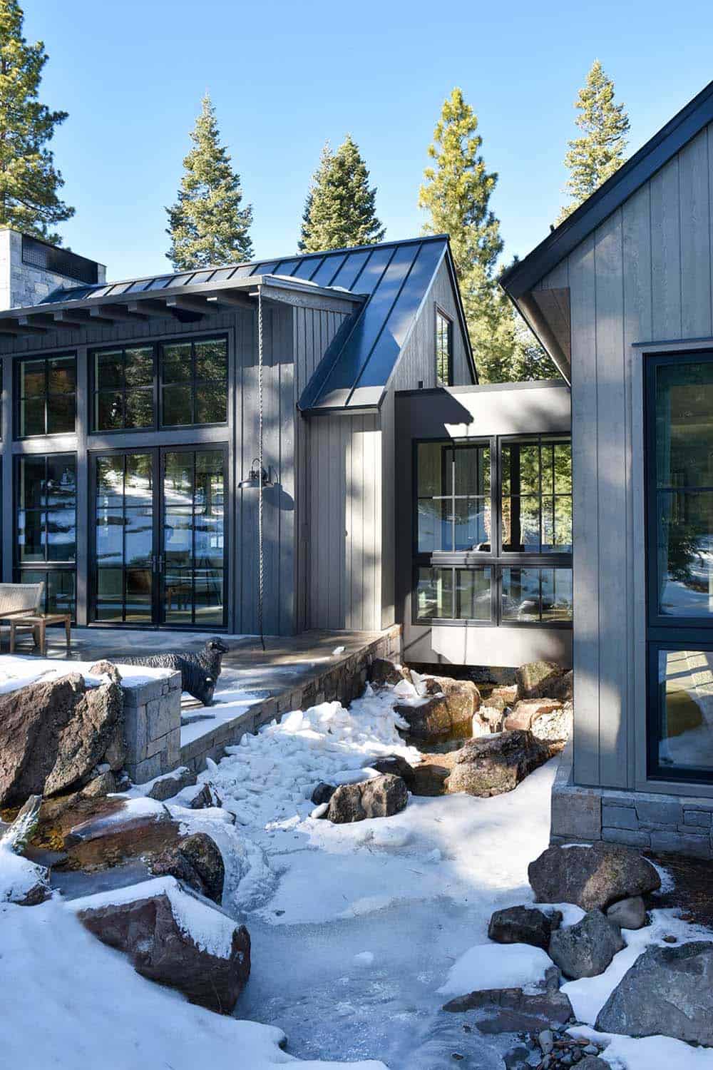 Snow-covered exterior connecting two gabled wings with stone-lined creek