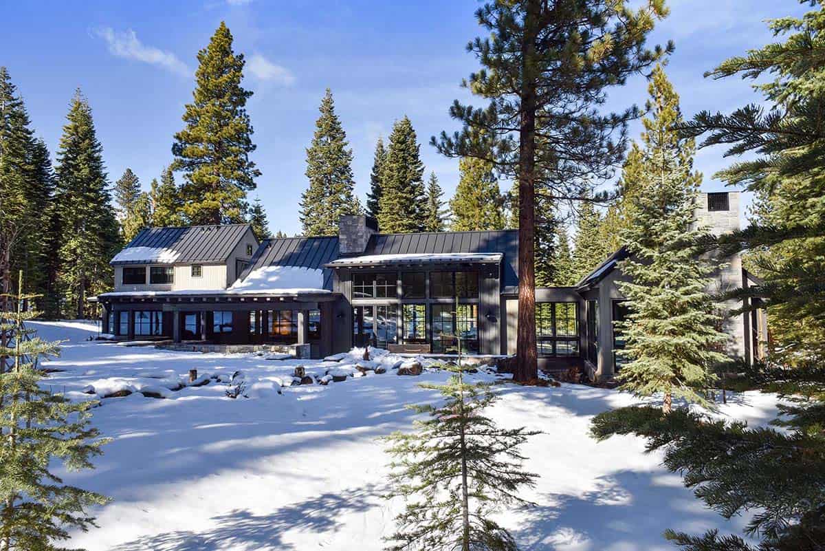 Wide snowy exterior view of the mountain home framed by pine trees