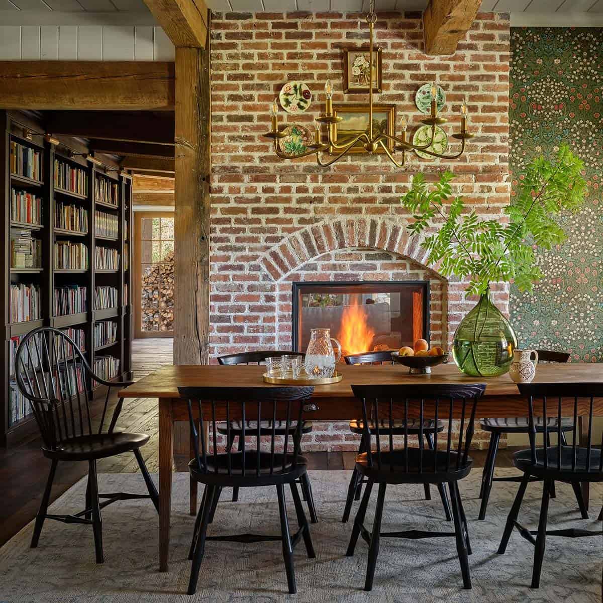Dining table beneath brick fireplace and built-in bookshelves