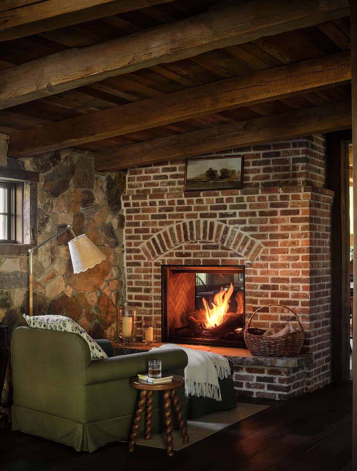 Reading chair beside brick fireplace with basket of logs