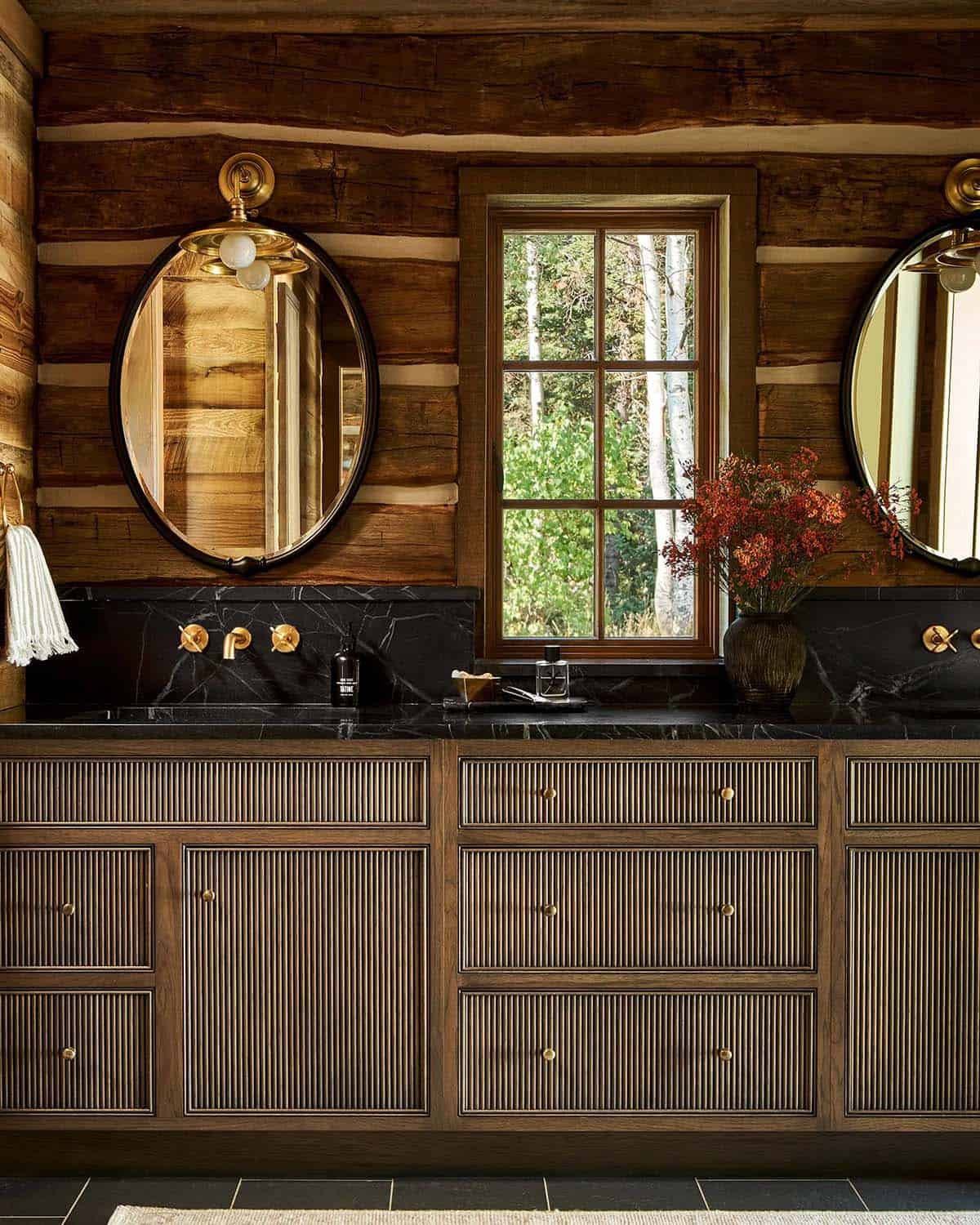 Log cabin bathroom with dual oval mirrors and black countertops