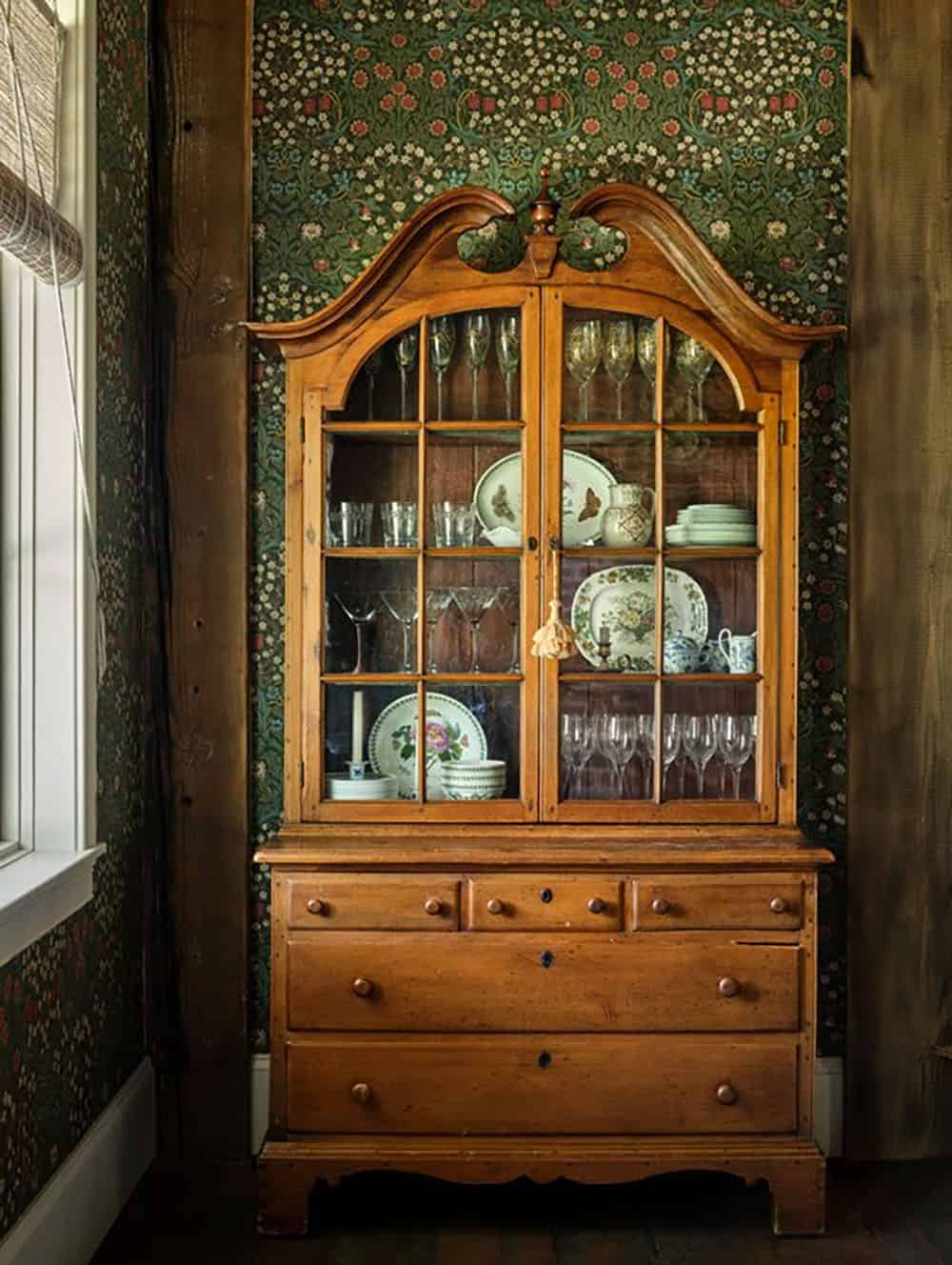 Glass-front cabinet against green floral wallpaper