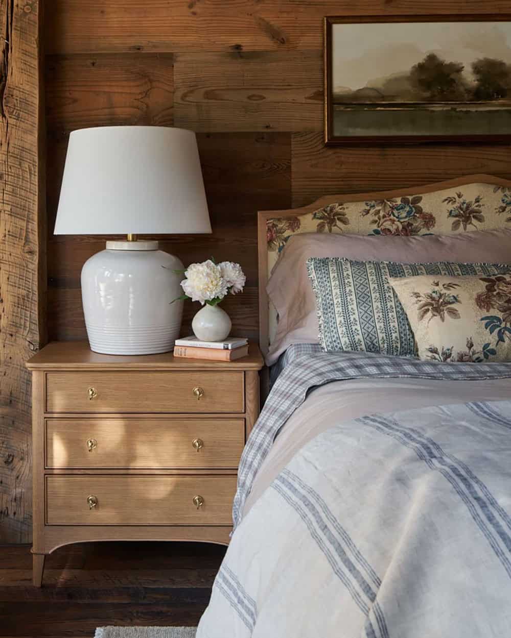 Bedside table with ceramic lamp beside floral upholstered headboard