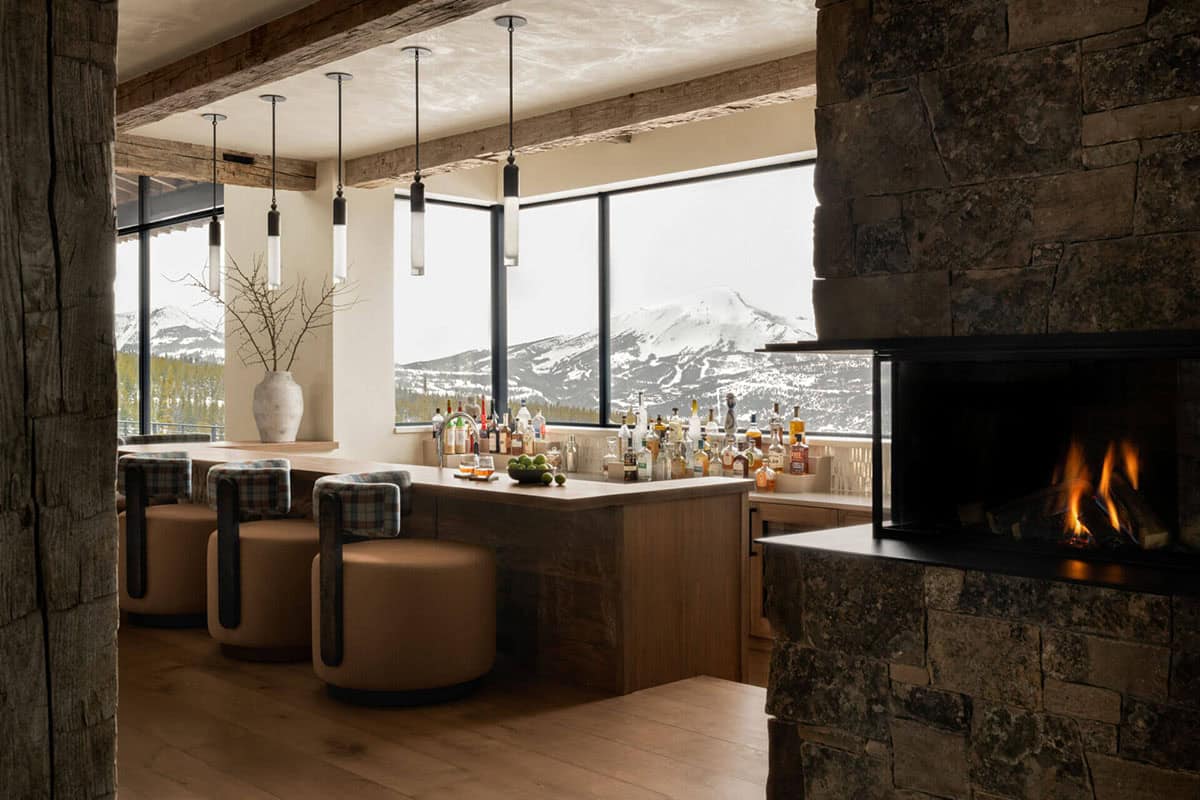 Wet bar and stone fireplace framed by mountain views