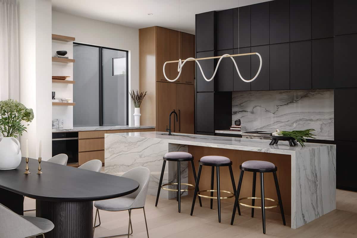 Black cabinetry kitchen with waterfall marble island and sculptural pendant light