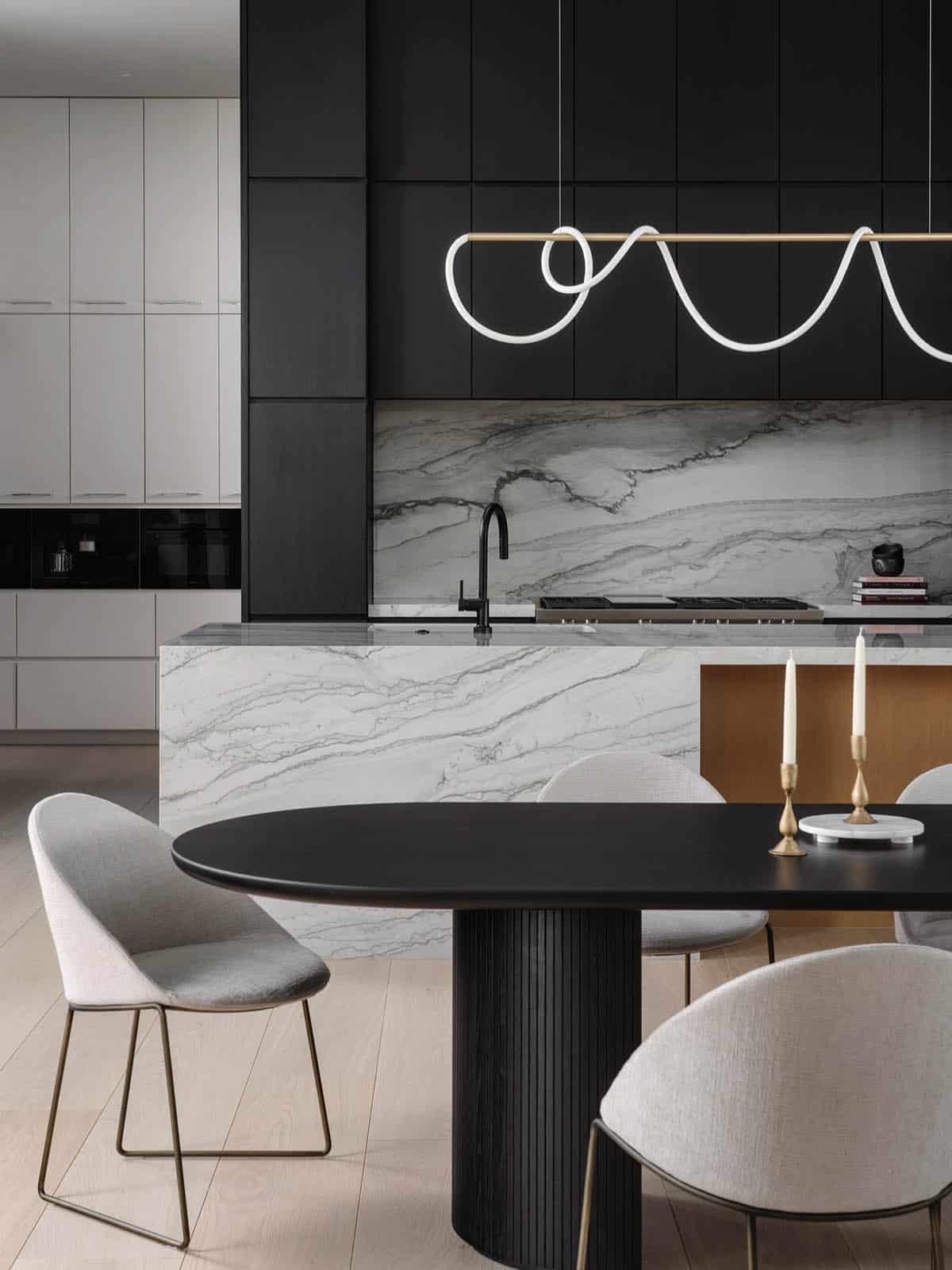 Black kitchen cabinetry with marble slab backsplash and oval dining table