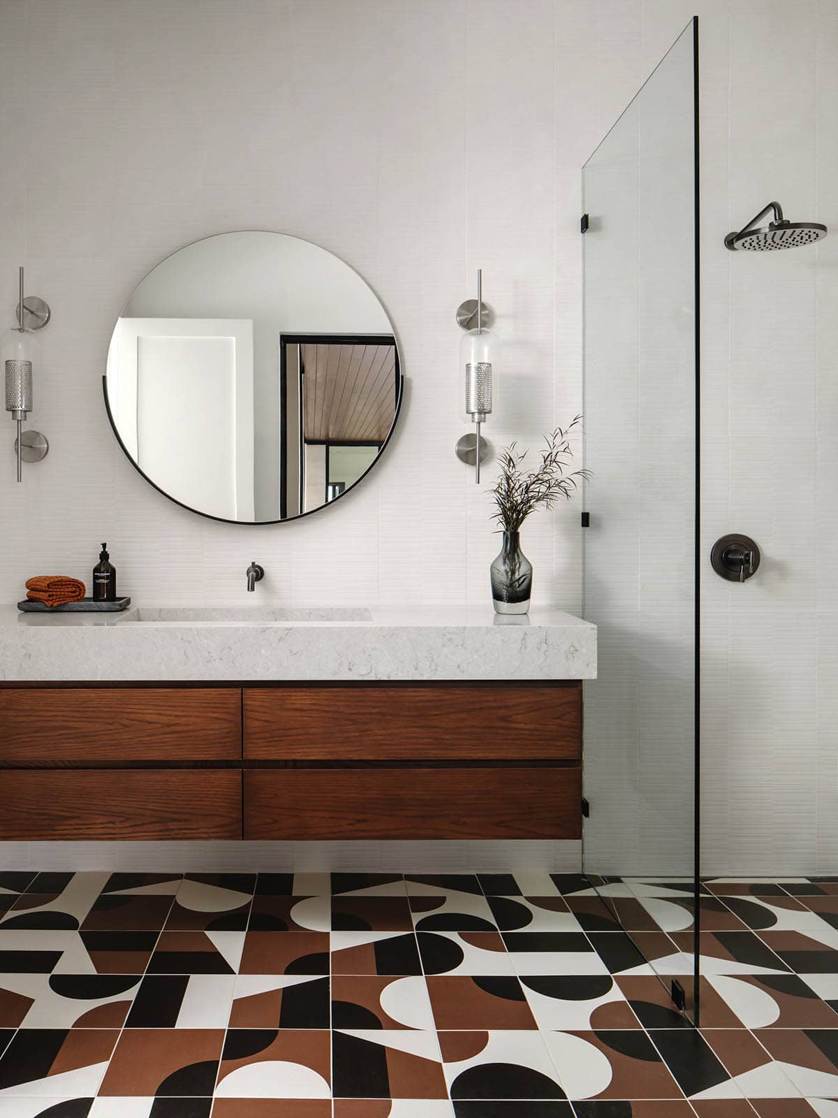 Geometric tile bathroom floor beneath a floating walnut vanity and round mirror