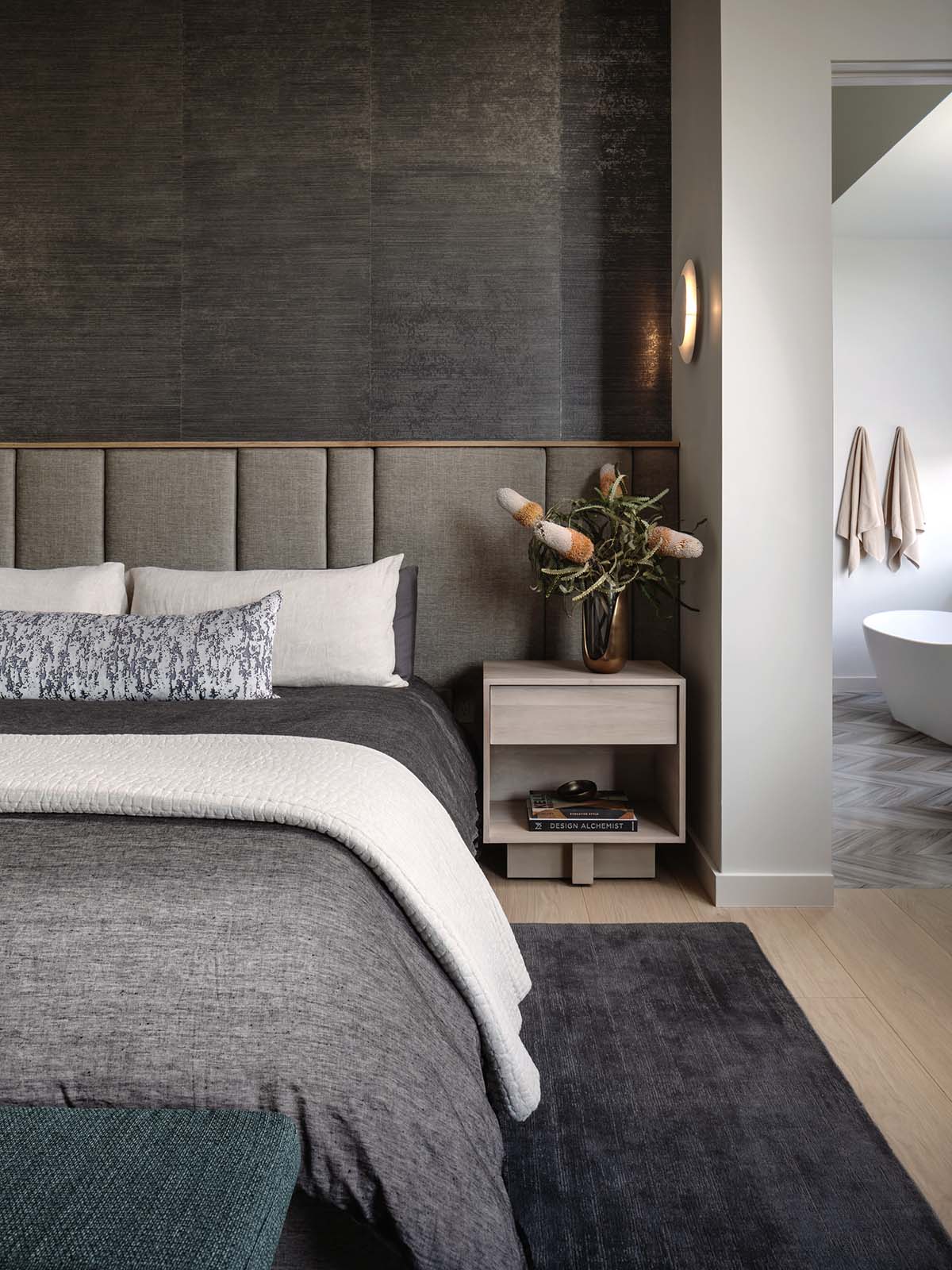 Upholstered channel headboard beside a wood nightstand and bathroom doorway