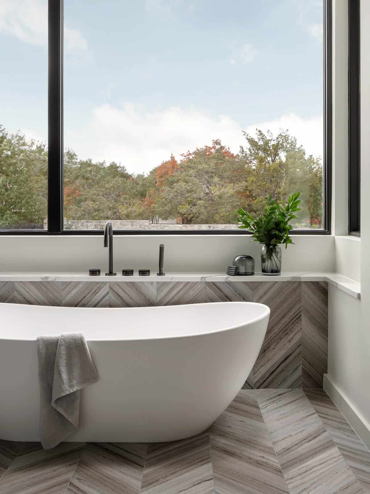 Freestanding tub beneath a picture window with chevron tile surround