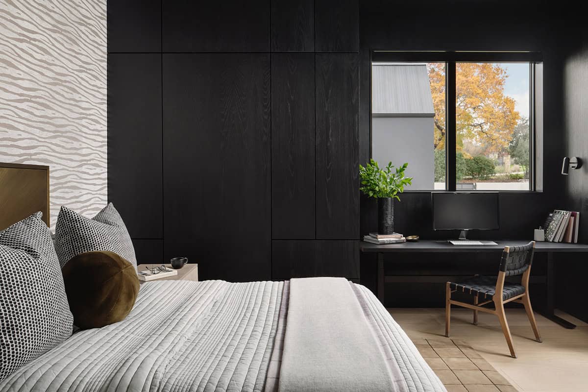 Black paneled bedroom with built-in desk and woven leather chair