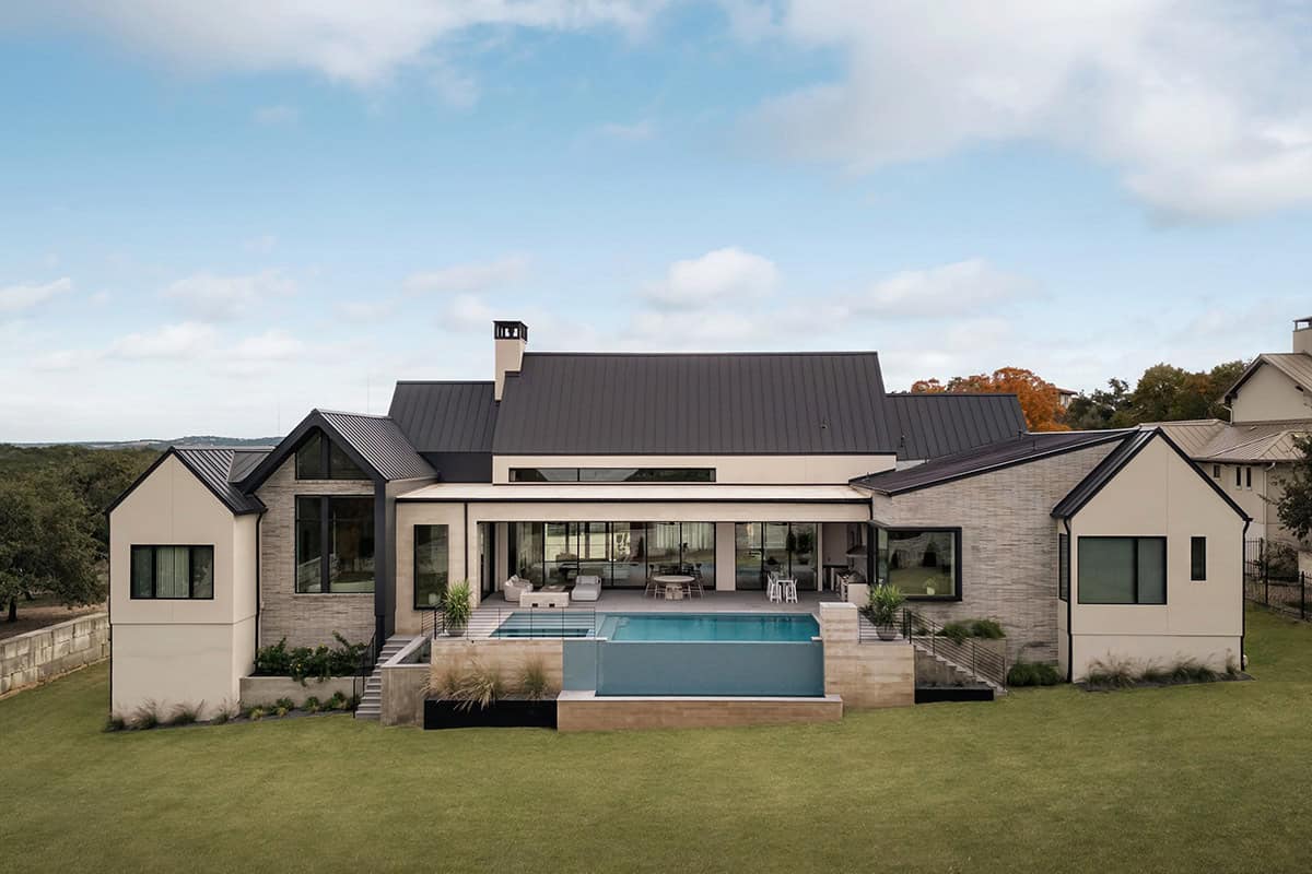 Aerial rear view of gabled home with vanishing-edge pool and hill views