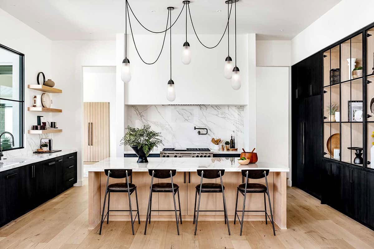 Kitchen island with black stools beneath cluster of glass pendant lights