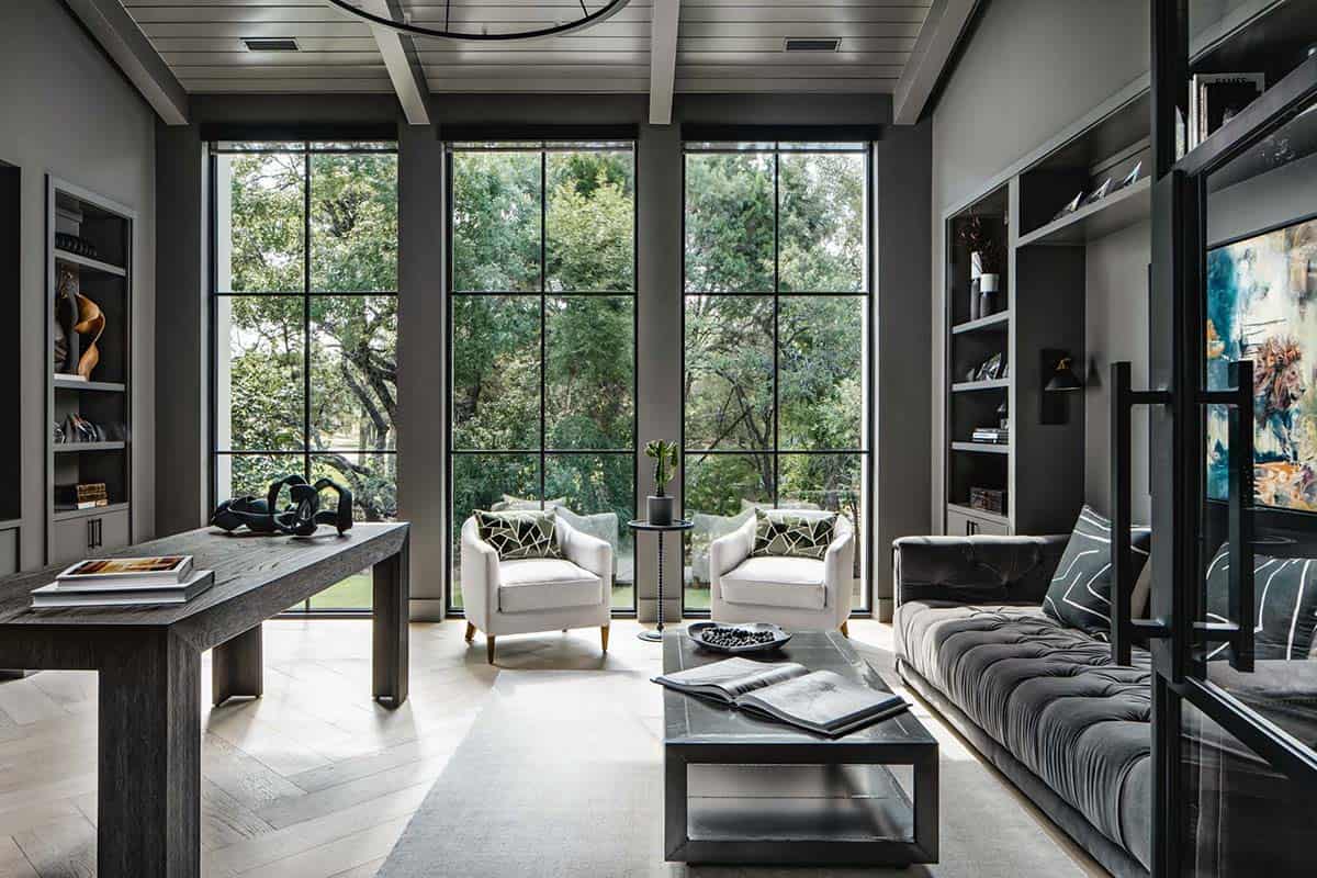 Home office seating area facing wooded backyard through tall windows