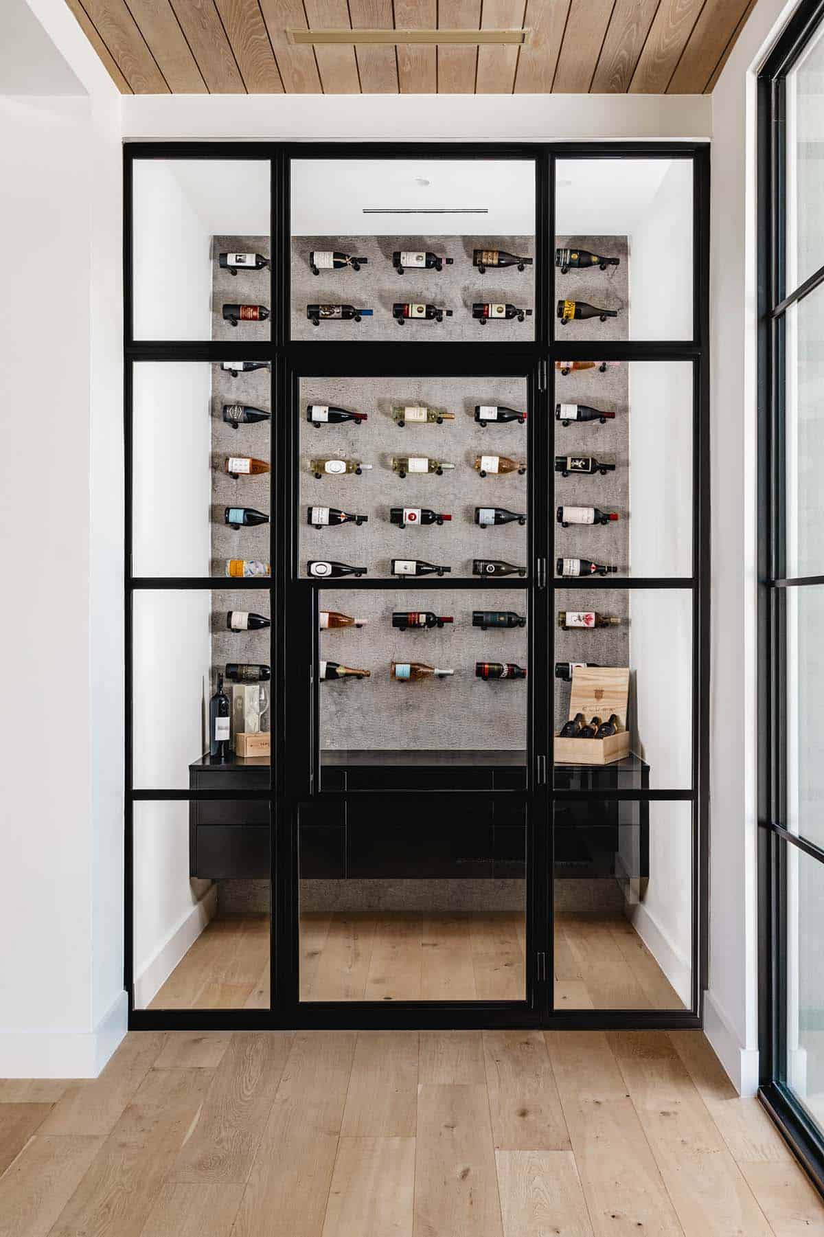Glass-enclosed wine room with wall-mounted bottles and black cabinetry