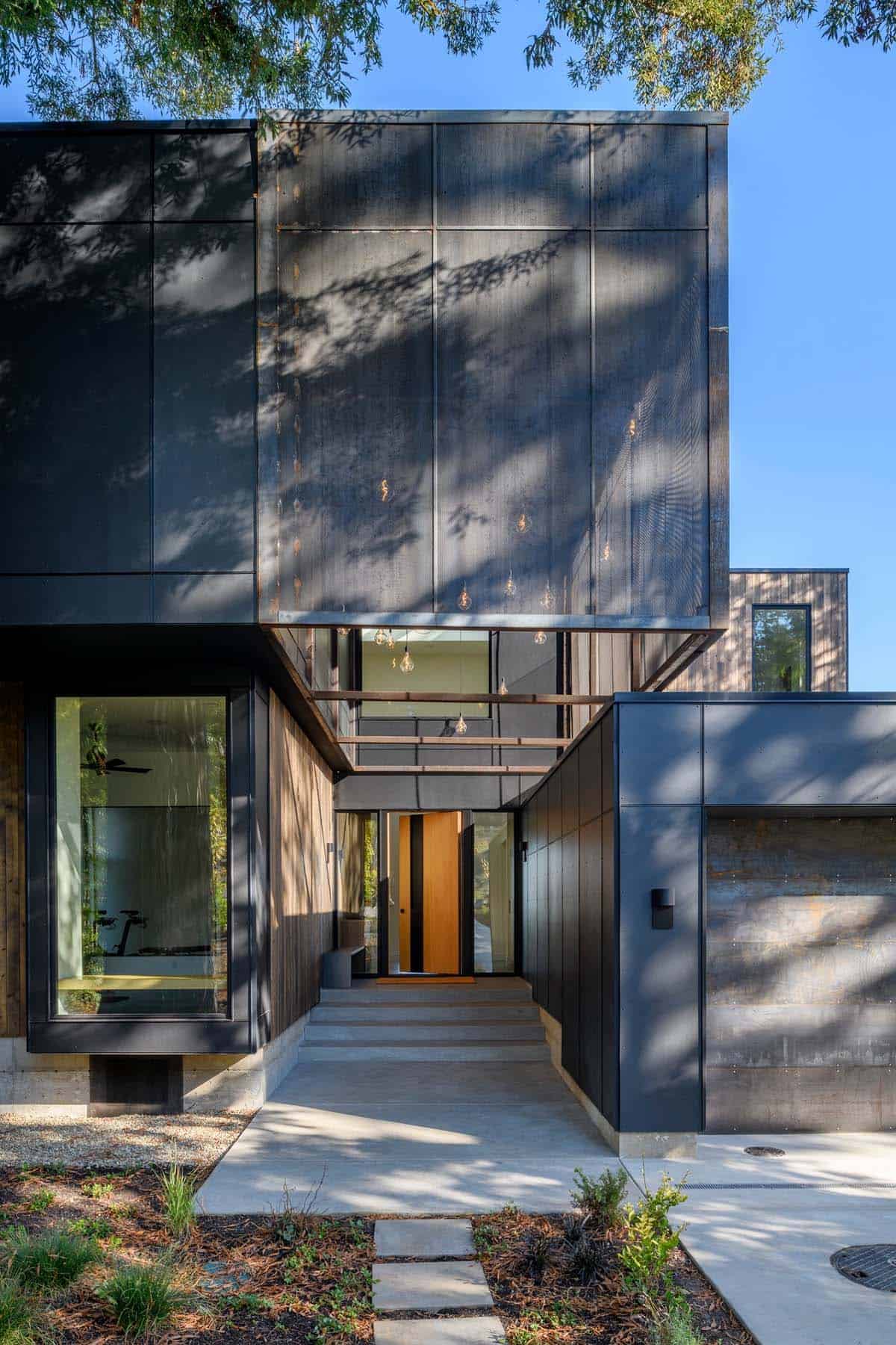 Dark metal-clad entry facade shaded by mature evergreen trees