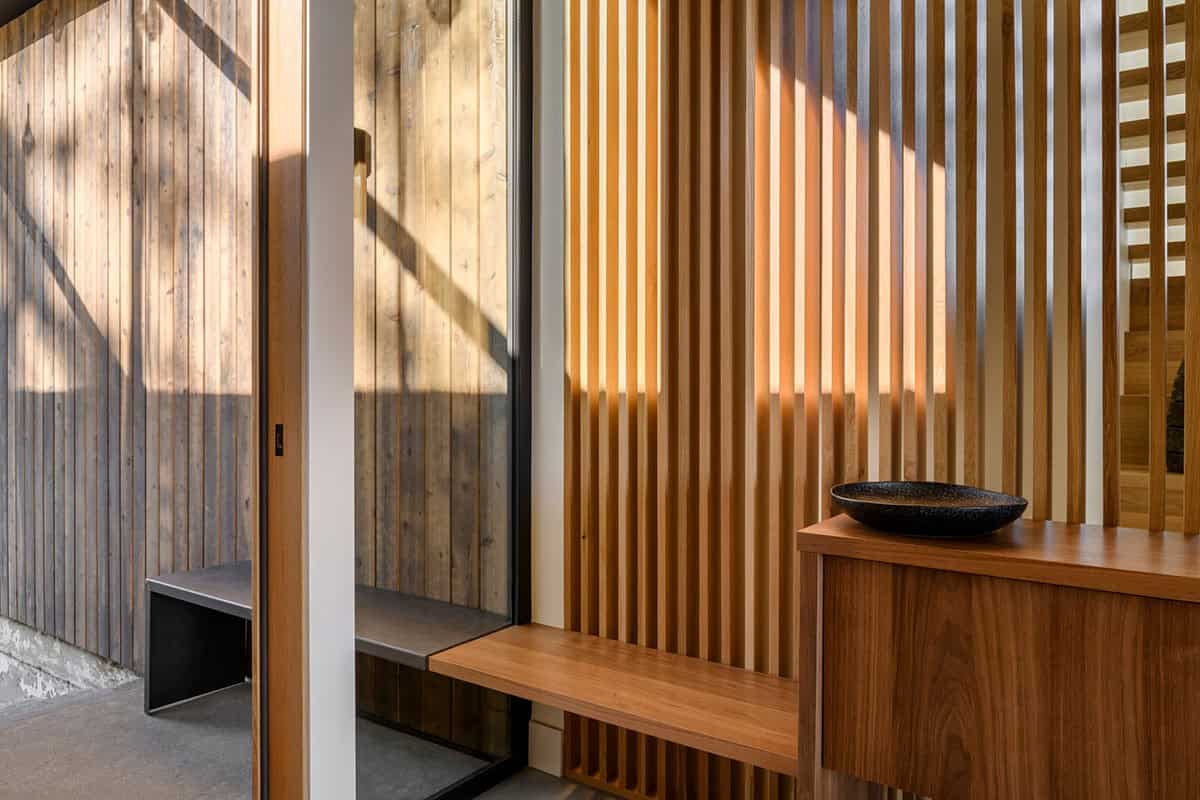 Vertical cedar slats frame glass door beside walnut entry bench