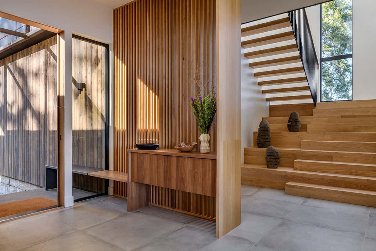 Wood slat partition separates entry from oak staircase and console