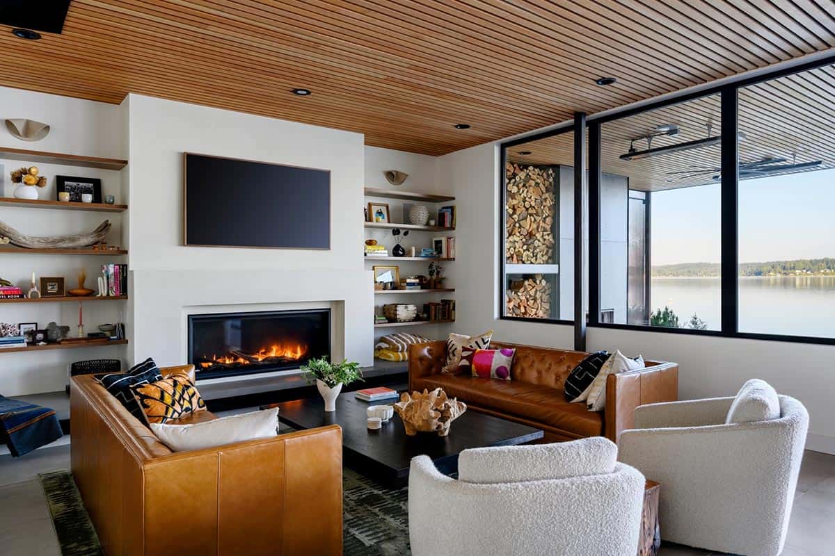 Leather sofas surround fireplace with lake views through corner windows