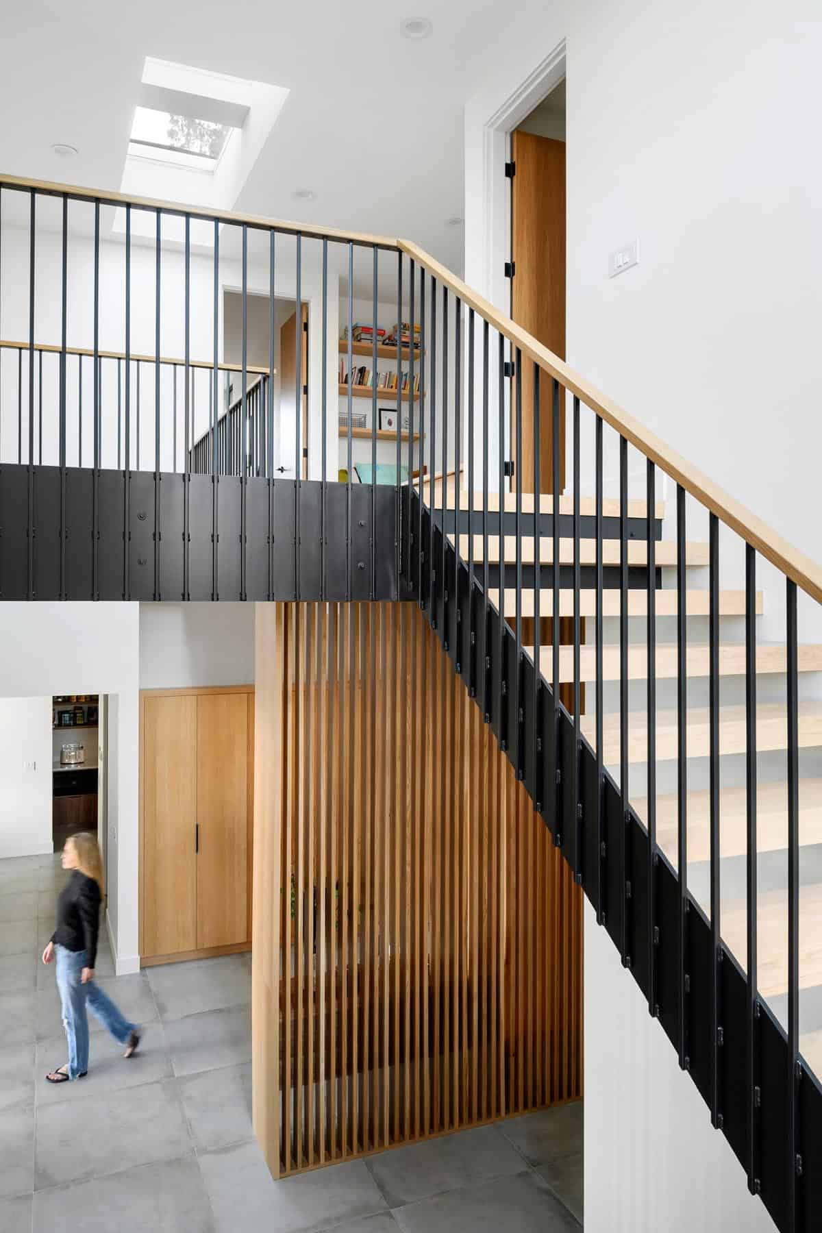 Black metal stair railing overlooks wood slat storage nook below