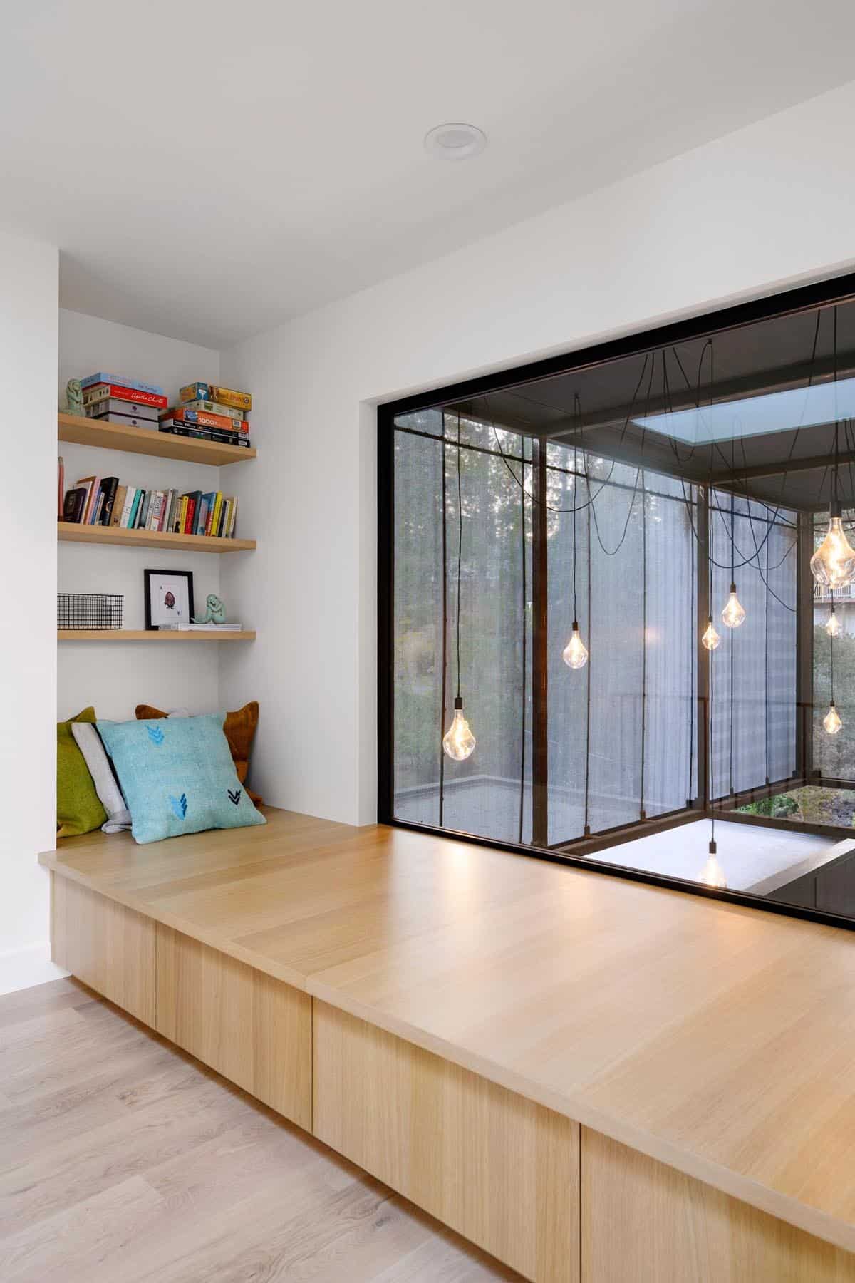 Built-in window seat with bookshelves overlooking glass breezeway lights