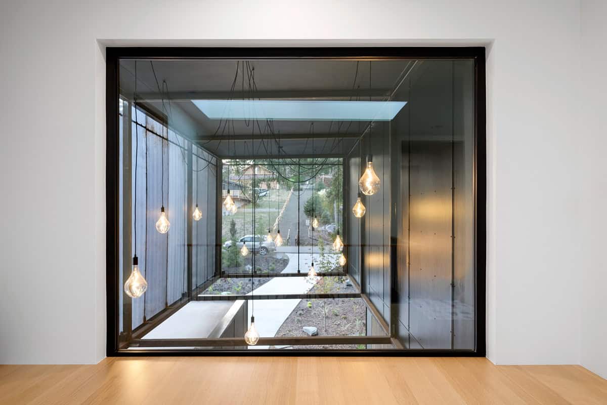 Glass breezeway ceiling hung with pendant bulbs above concrete path