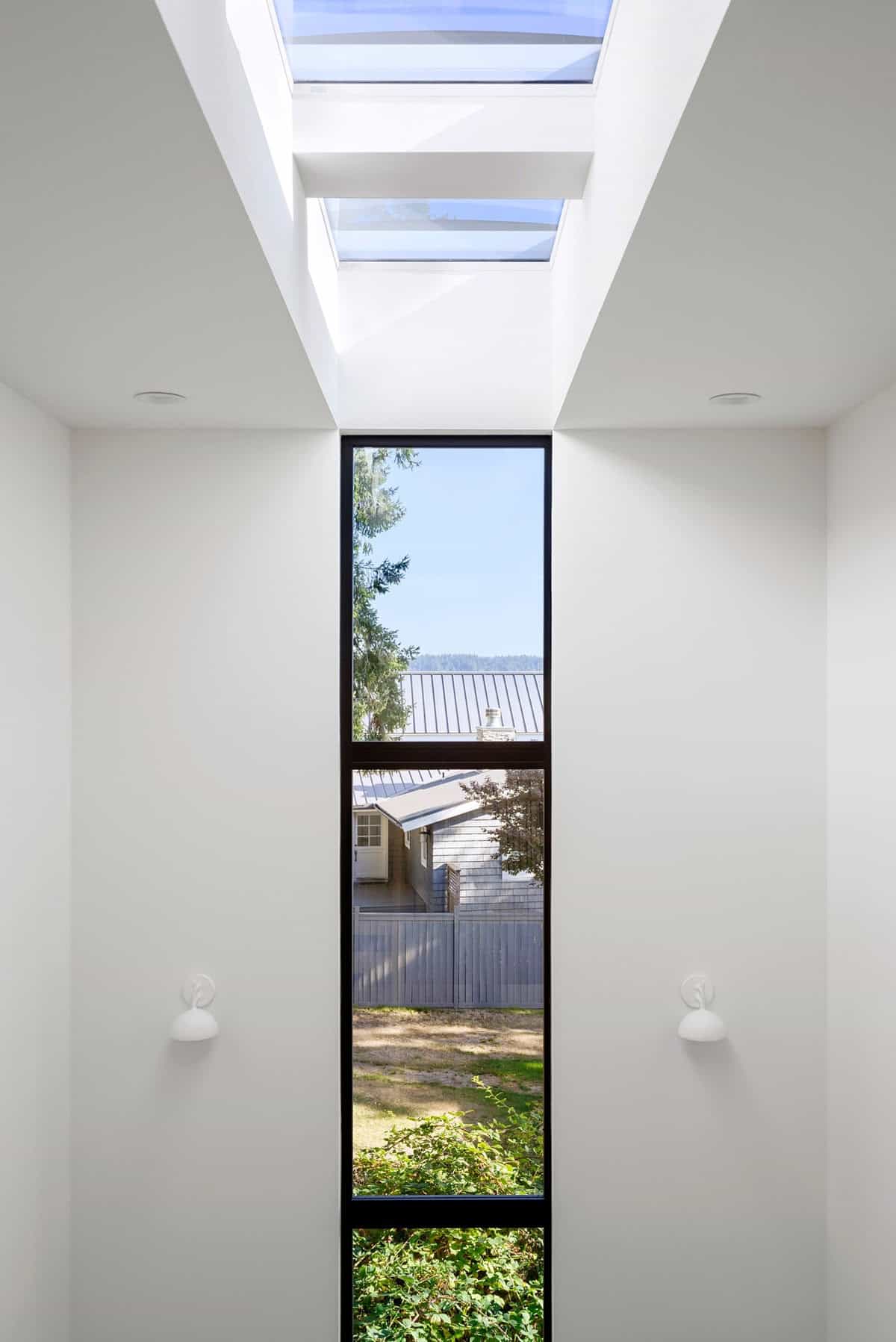 Narrow skylight window frames neighboring rooftops and greenery below