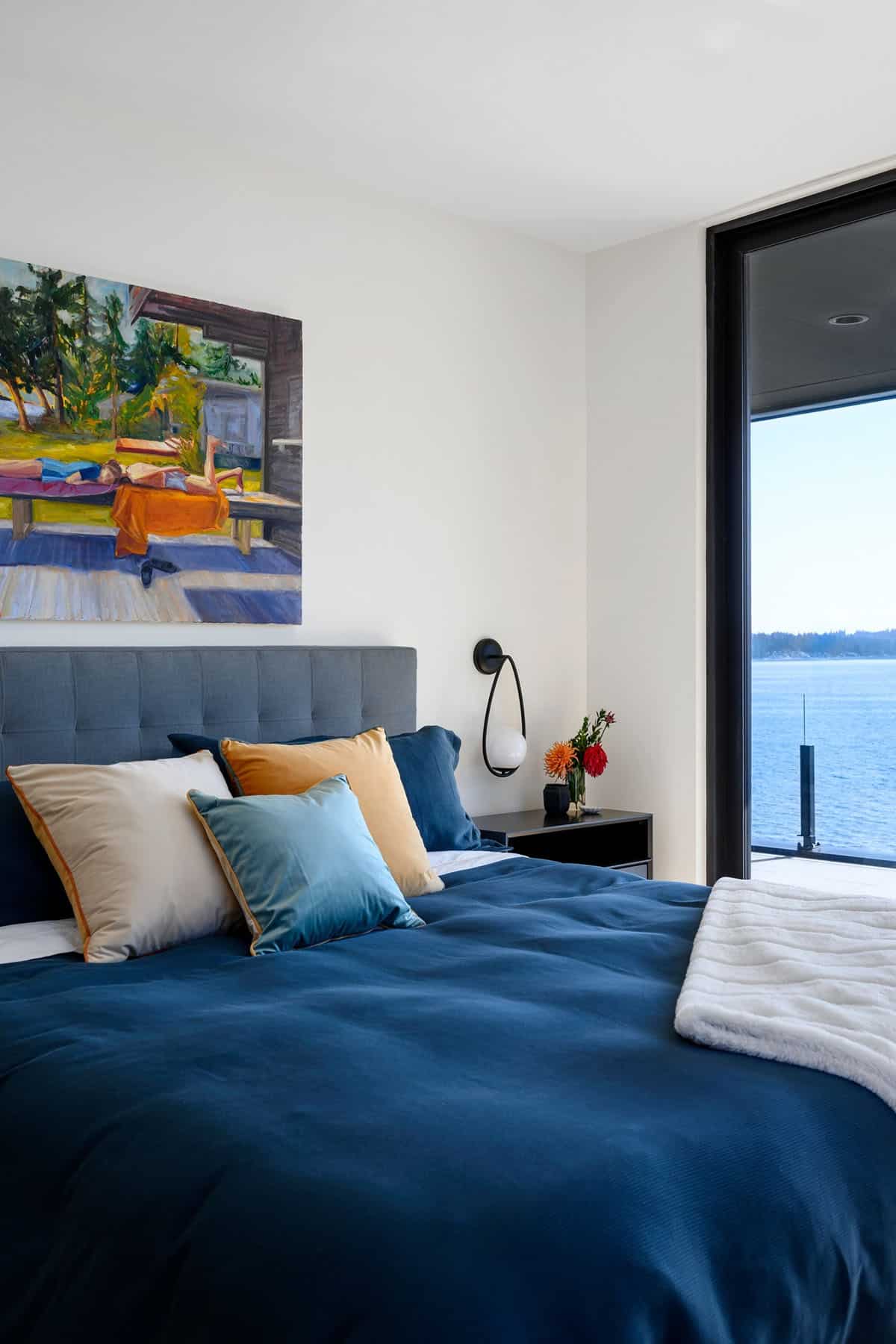 Blue bedding and painting overlook water view through glass door