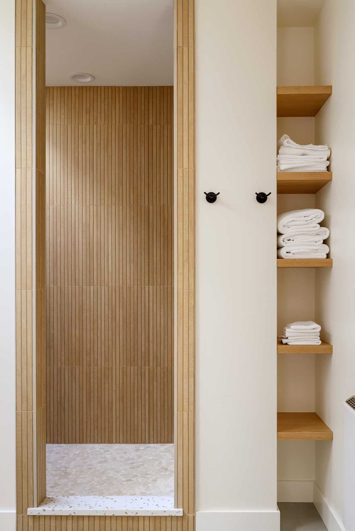 Wood slat shower nook beside folded towels on floating shelves