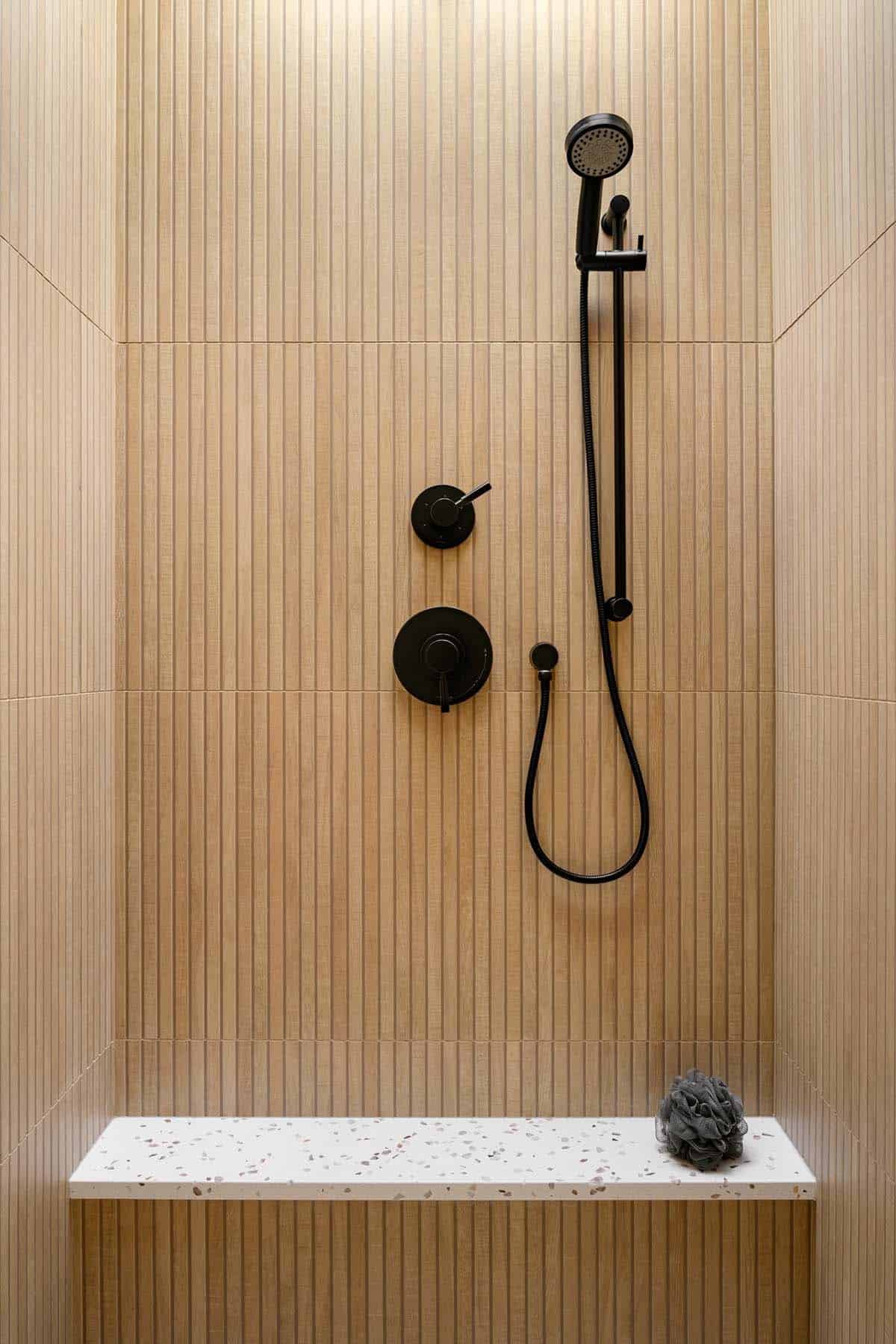 Black fixtures against wood slat shower wall with terrazzo bench