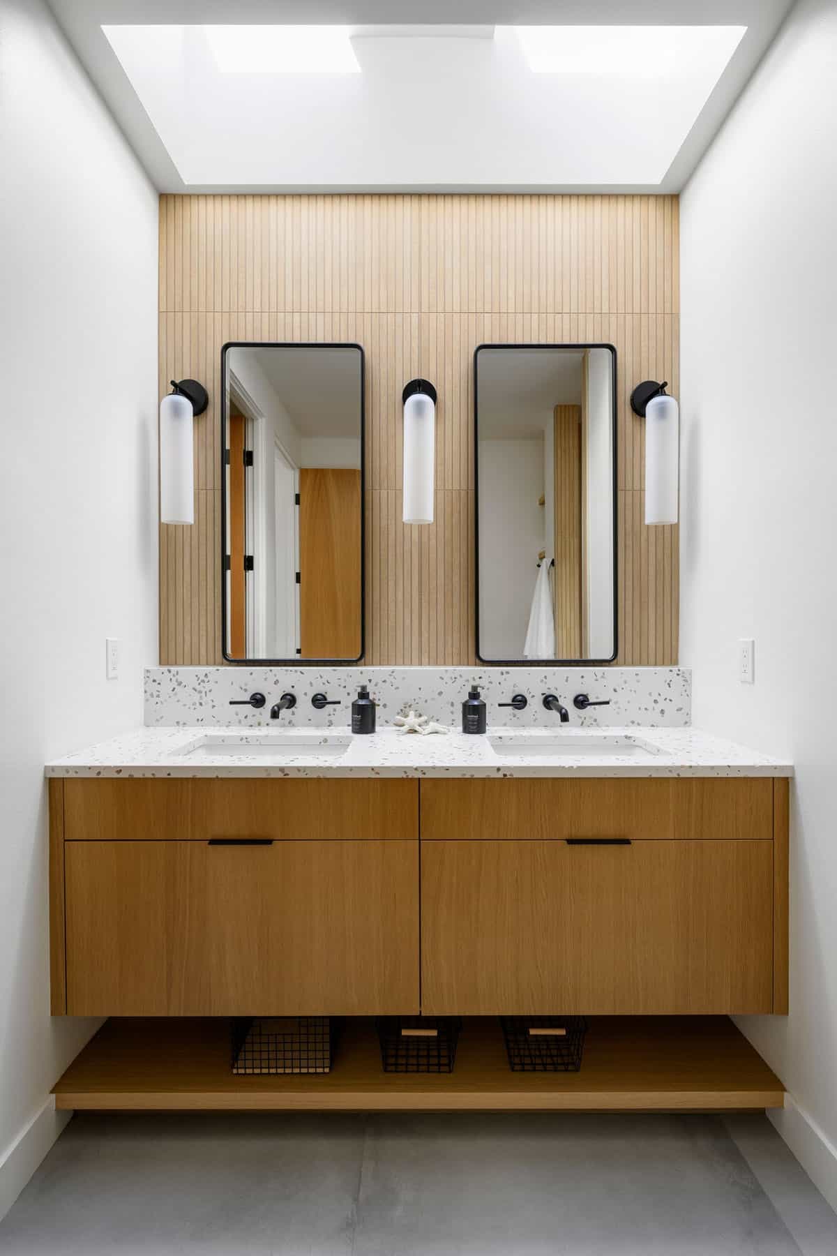 Double vanity with terrazzo counter under skylight and wood paneling