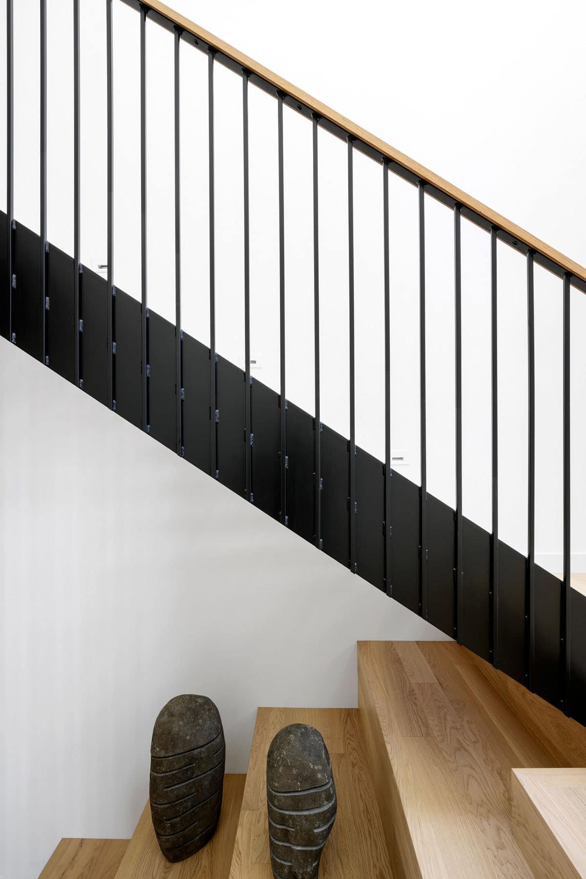 Stone sculptures rest on oak stair treads beneath black railing