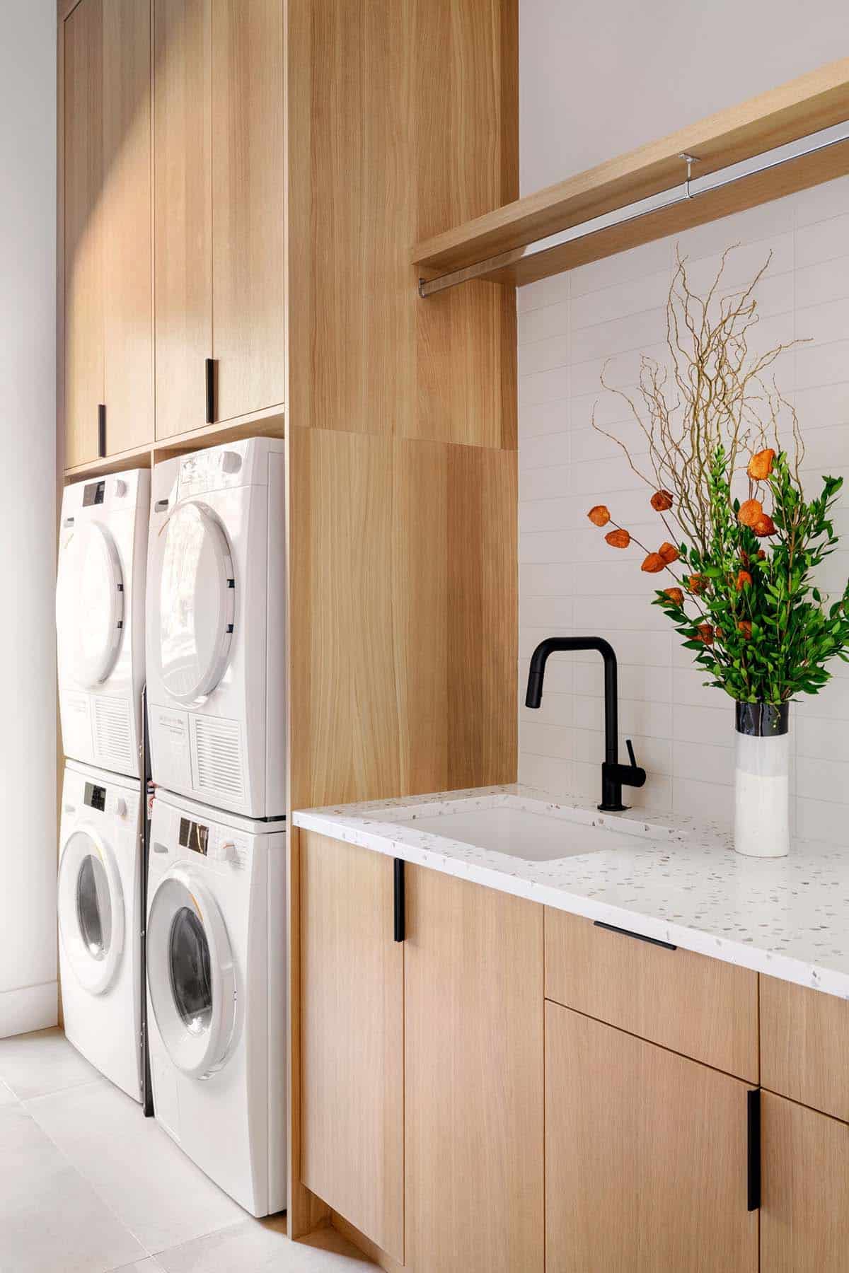 Wood-paneled laundry room with stacked washers and terrazzo sink counter